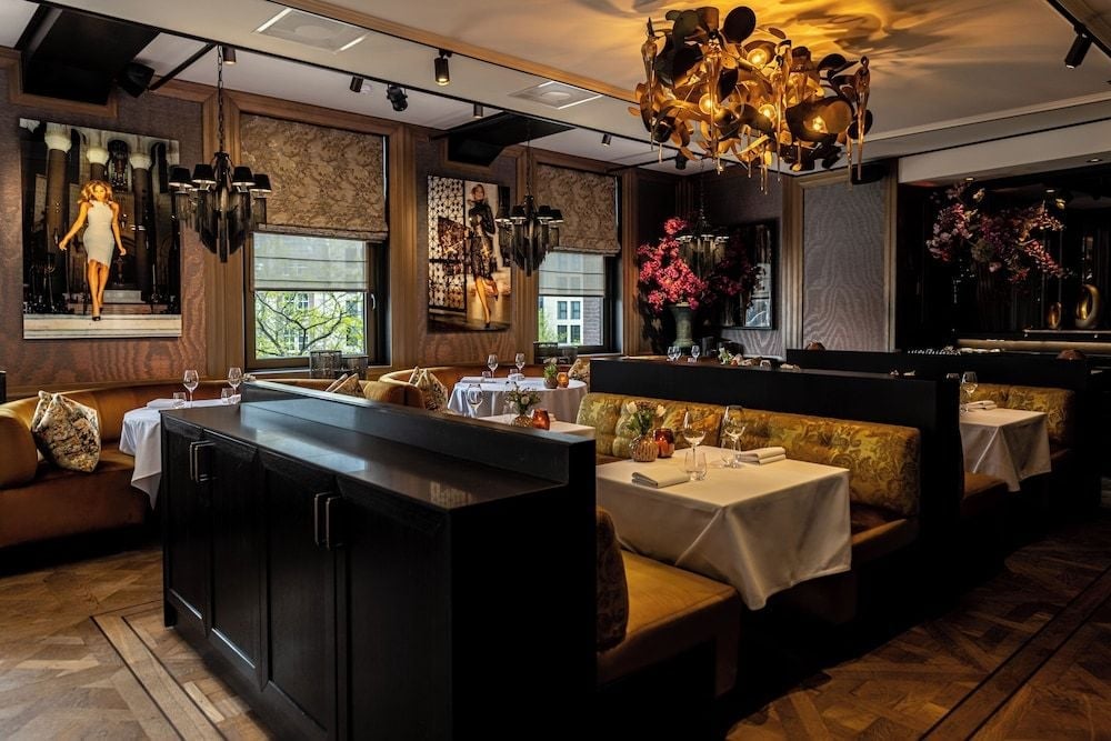 Golden banquette seating and dramatic florals create an intimate dining atmosphere, where crystal stemware catches warm light from the ornate chandelier above.