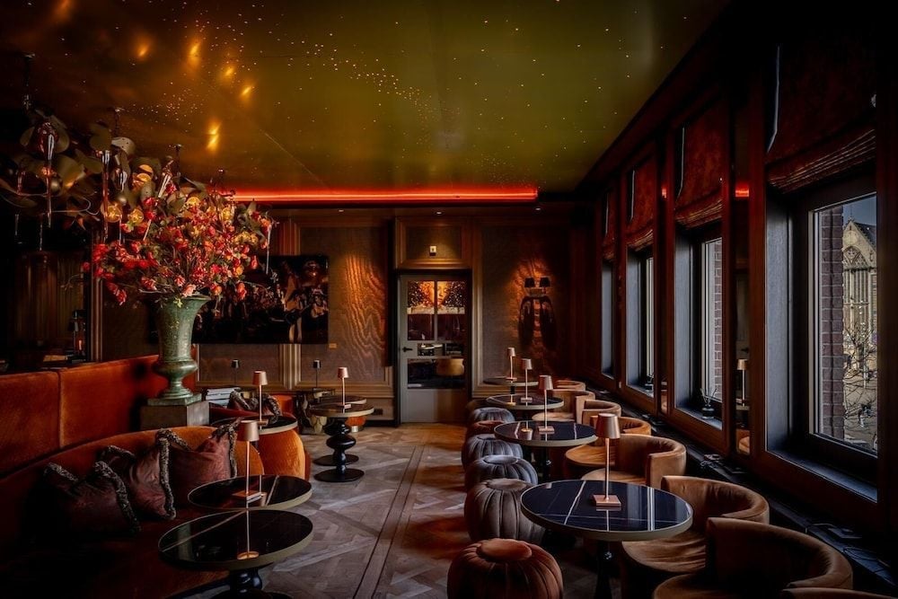 Moody amber lighting bathes plush velvet seating and rich wood paneling, where starlit ceilings and autumn florals create an intimate cocktail sanctuary.
