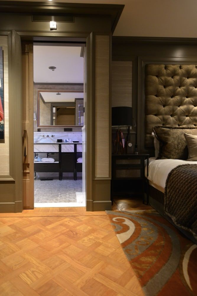 Sumptuous tufted leather headboards and rich parquet floors create an intimate sanctuary, while the marble-clad ensuite beckons through elegant doorways framed in burnished wood.