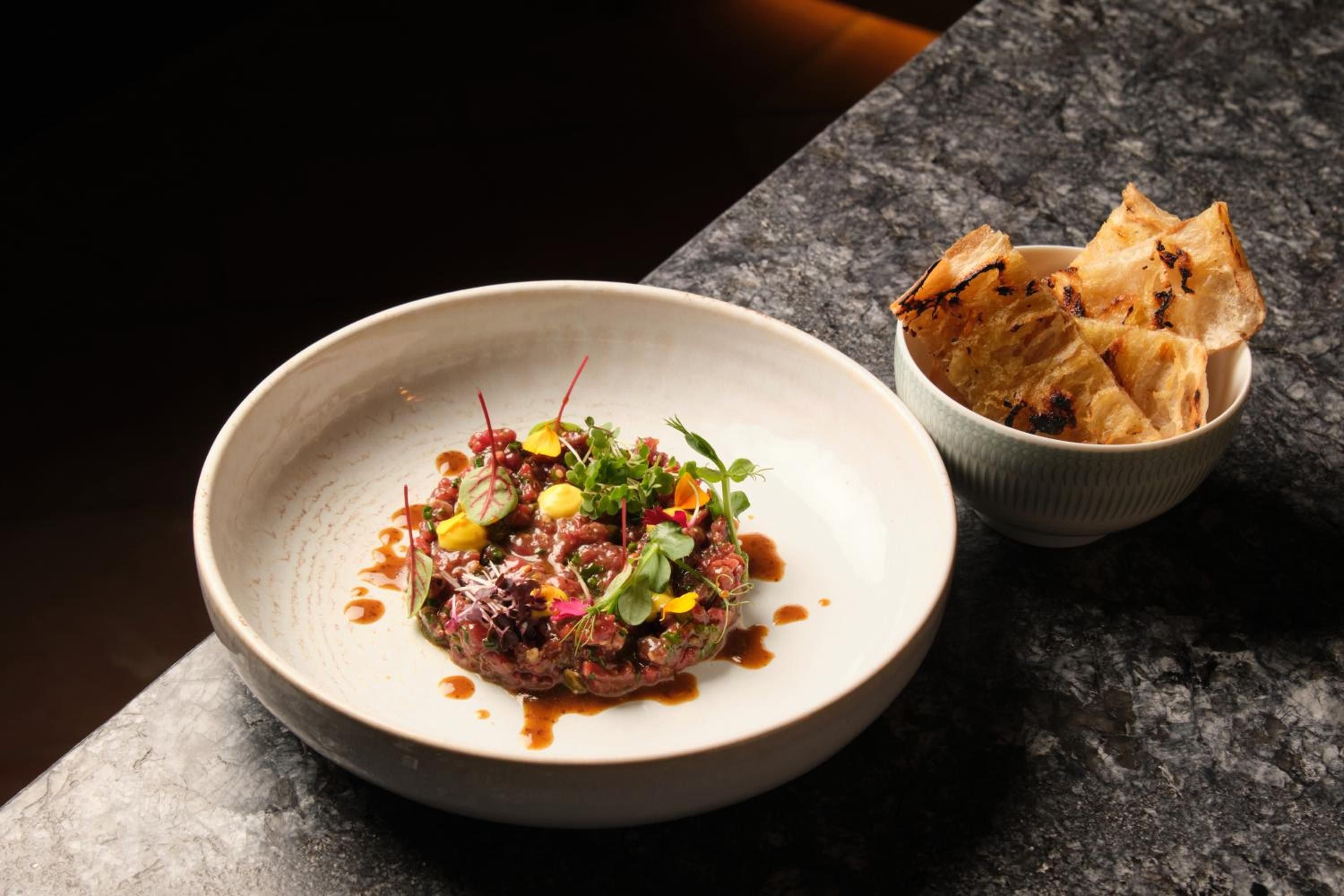 Artfully plated beef tartare adorned with microgreens and vibrant garnishes arrives alongside house-made flatbread, showcasing the hotel's commitment to culinary artistry.