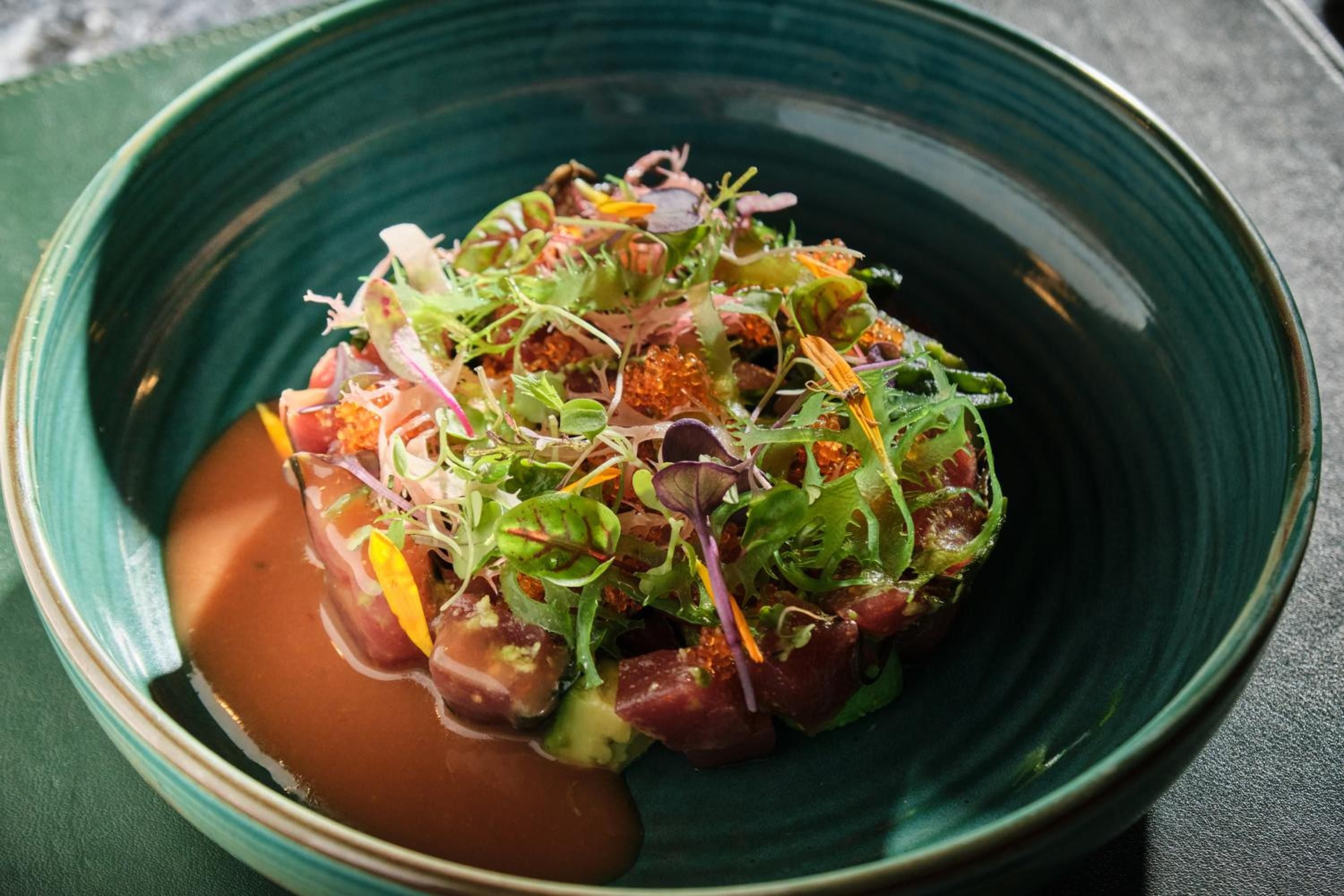 Seared tuna arrives artfully plated on emerald ceramics, crowned with delicate microgreens and vibrant edible flowers—a feast for both palate and eyes.