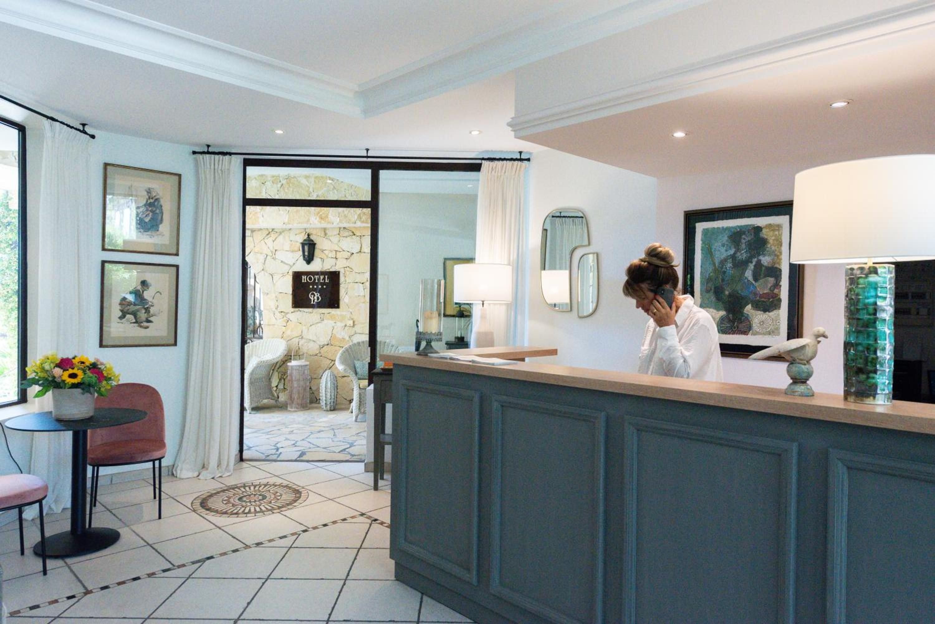 Stone floors and sage-green paneling create an intimate reception area where afternoon light filters through white curtains, revealing glimpses of the sun-dappled terrace beyond.