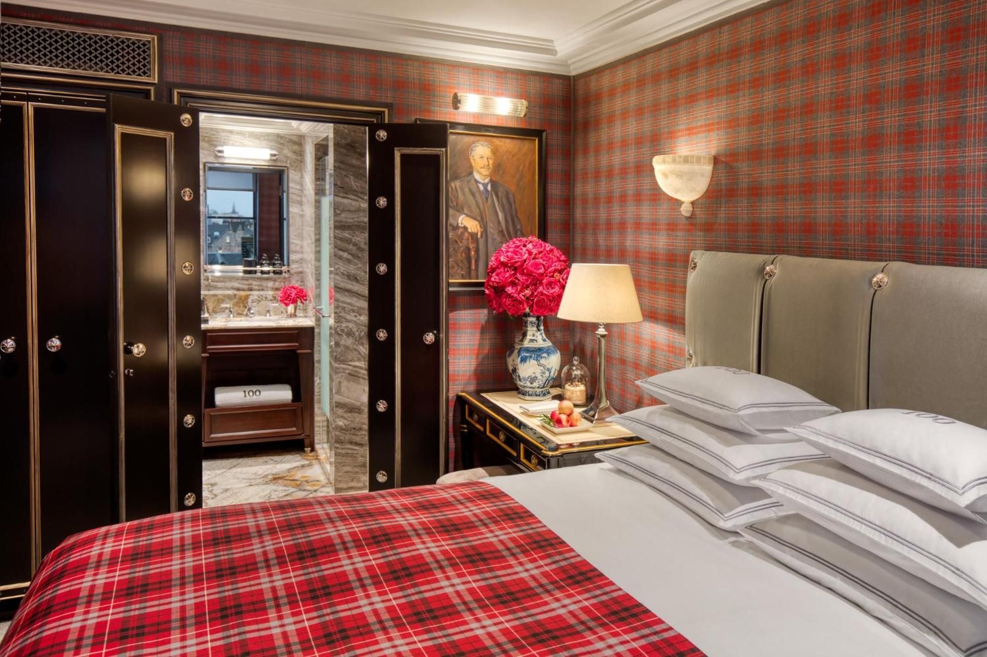 Plaid wallpaper and a classical portrait create Highland elegance in this sophisticated suite, where marble glimpses through dark wood paneling suggest old-world Scottish luxury.