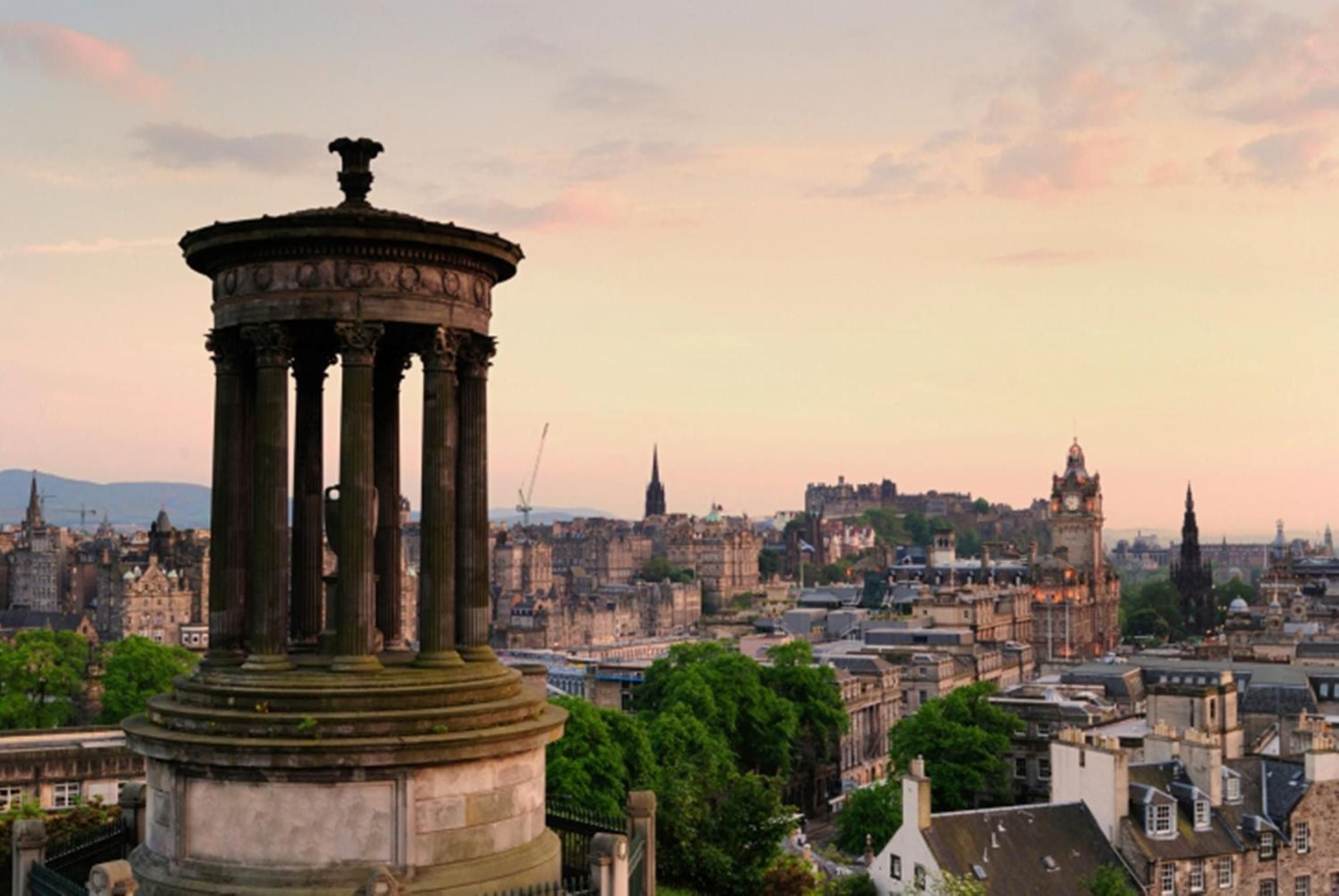 Golden hour light bathes Edinburgh's historic skyline from Calton Hill, where classical columns frame sweeping views of the castle and Old Town's ancient spires.