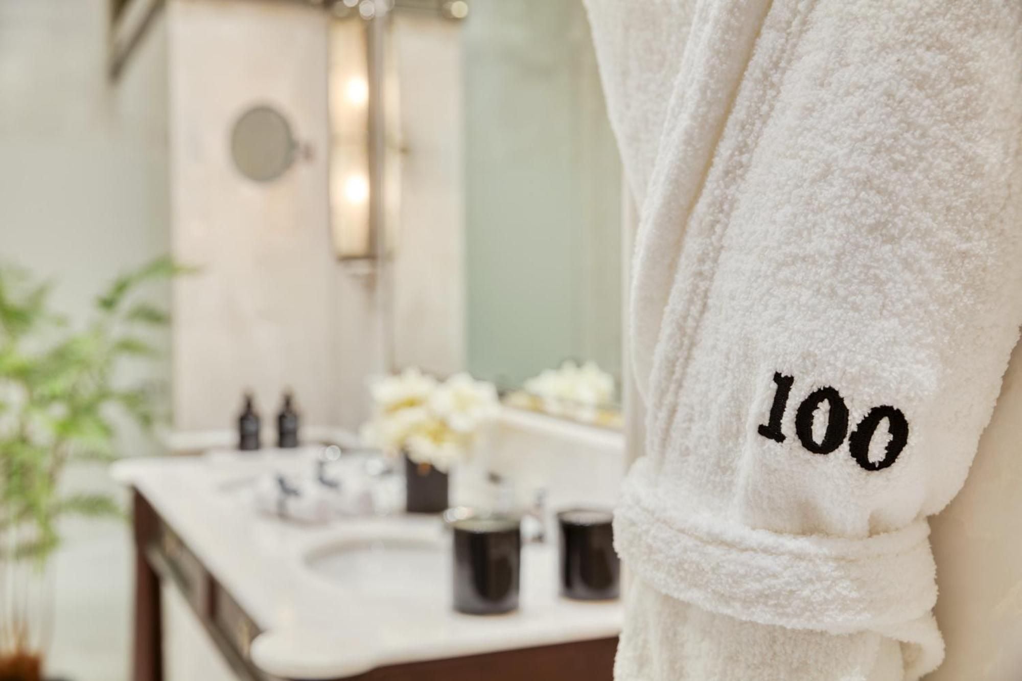 Plush terry robes embroidered with room numbers await guests in pristine marble bathrooms, where soft natural light creates an intimate spa-like sanctuary.