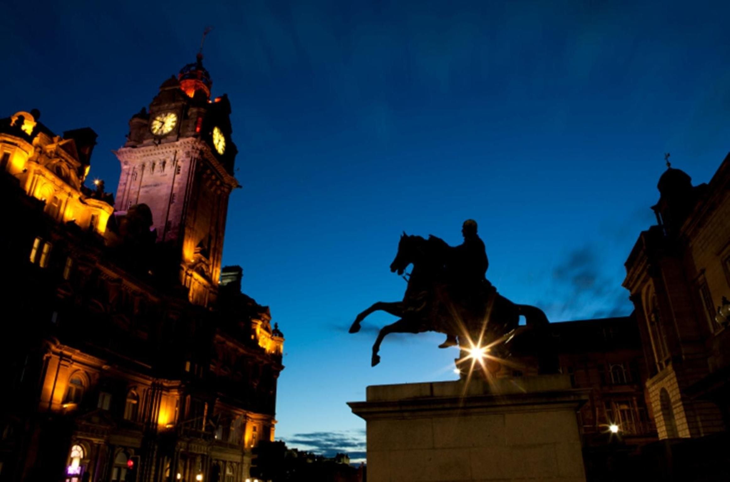 Golden hour illuminates Edinburgh's historic clocktower while an equestrian statue stands sentinel against the deepening twilight sky, creating a dramatic Scottish cityscape.
