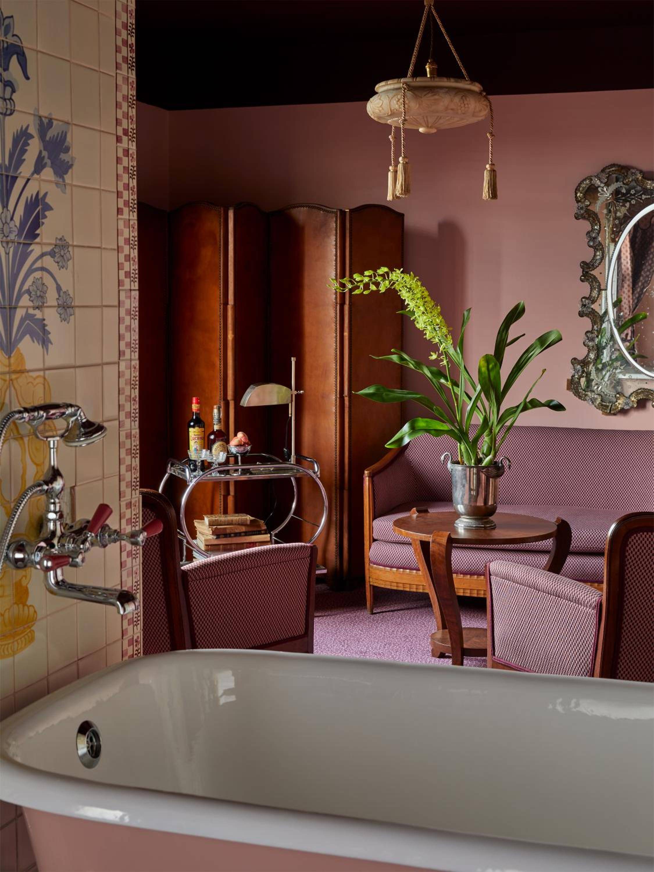Vintage brass fixtures and hand-painted tiles frame a soaking tub, while burgundy velvet seating and botanical touches create an unexpectedly luxurious bathing retreat.