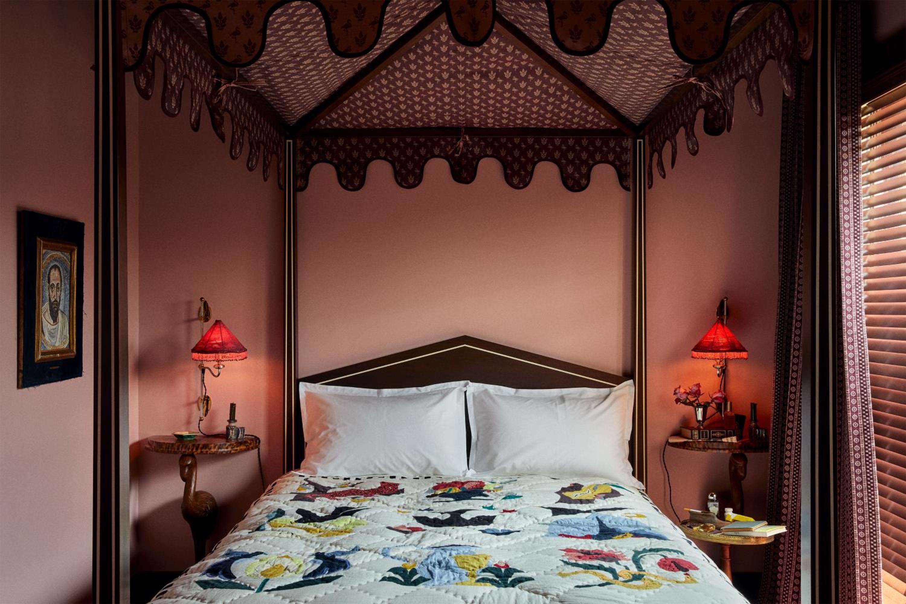 Ornate fabric canopy frames the bed like a Moroccan pavilion, while vibrant quilted botanicals and amber-glowing table lamps create an intimate, jewel-toned sanctuary.