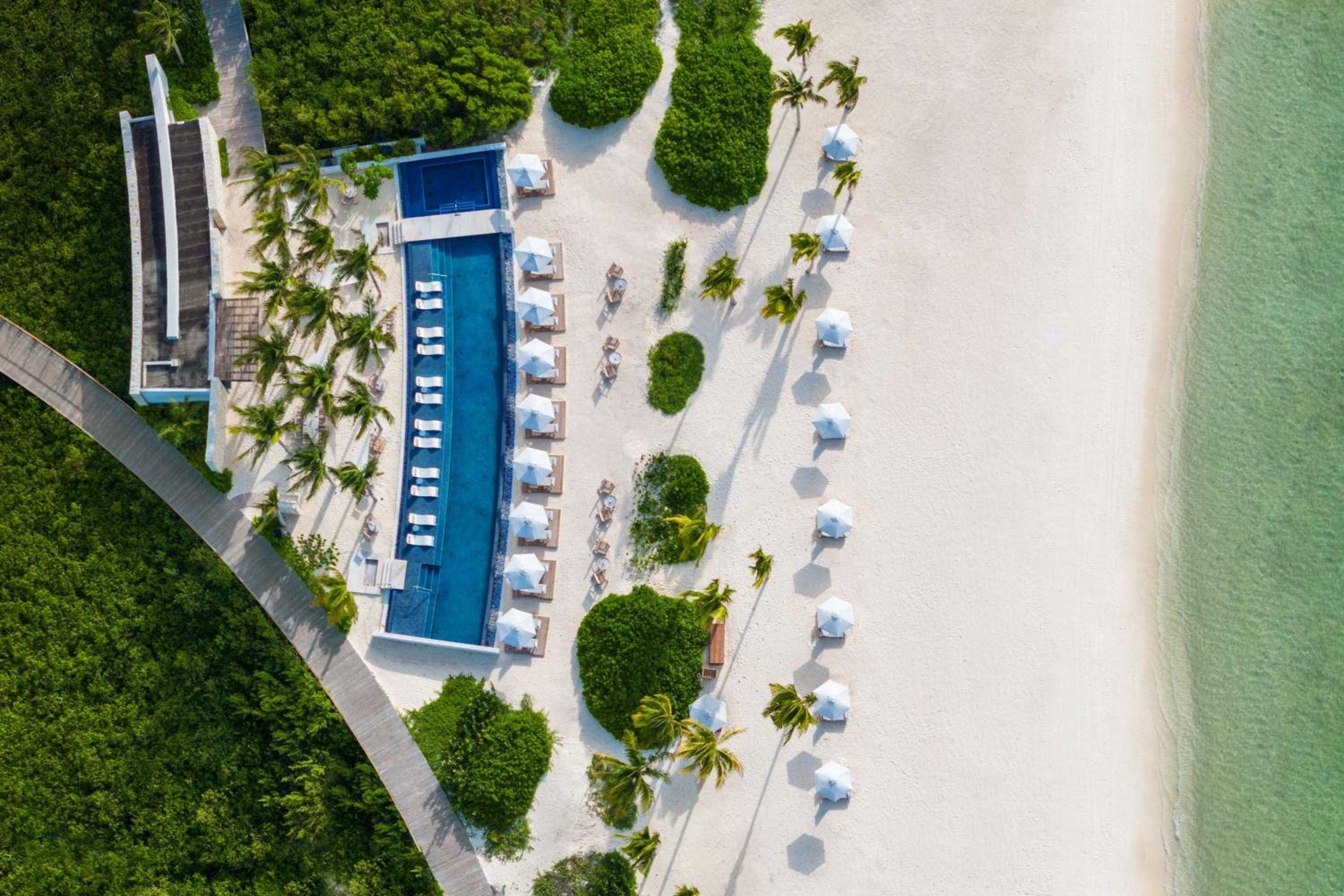 Crystalline waters meet powder-soft sand as Etéreo's infinity pool stretches toward the Caribbean, white umbrellas dotting the pristine beachfront like elegant sculptures.