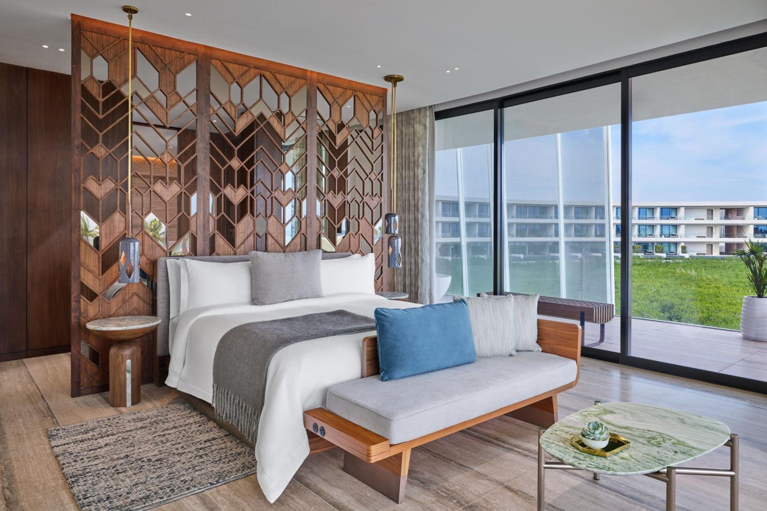 Geometric walnut screens frame the master suite, where contemporary Mexican design meets beachfront serenity through floor-to-ceiling windows overlooking manicured grounds.