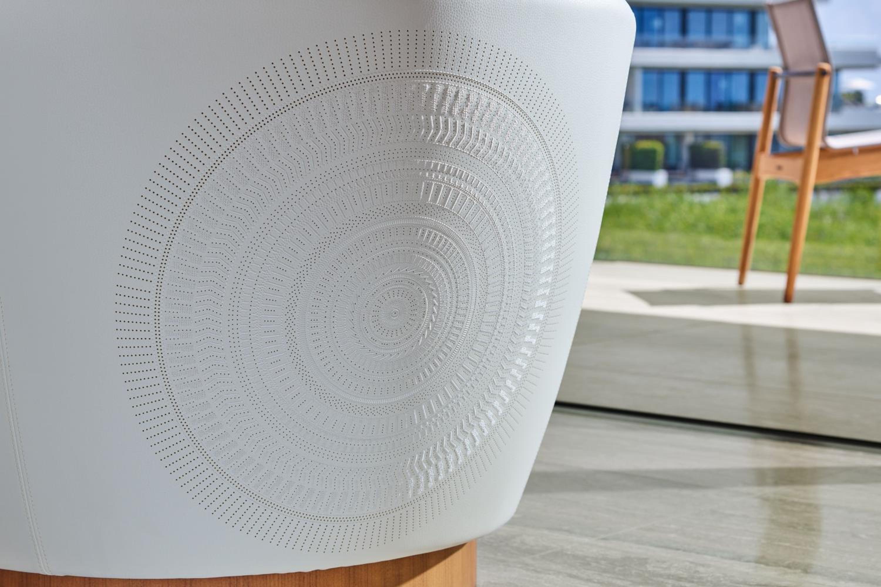 Perforated concentric circles create mesmerizing patterns on modern seating, where minimalist design meets artistic expression in sun-drenched common spaces overlooking verdant gardens.