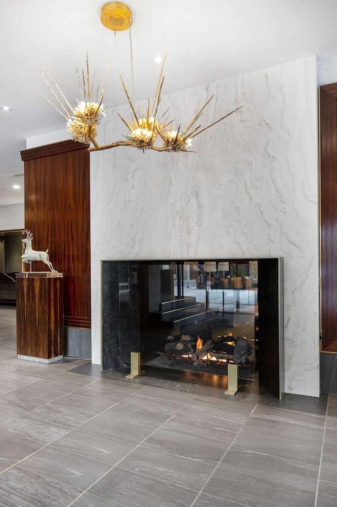 Sculptural chandeliers cast warm light over the marble-clad fireplace, where contemporary design meets alpine luxury in this striking common area.