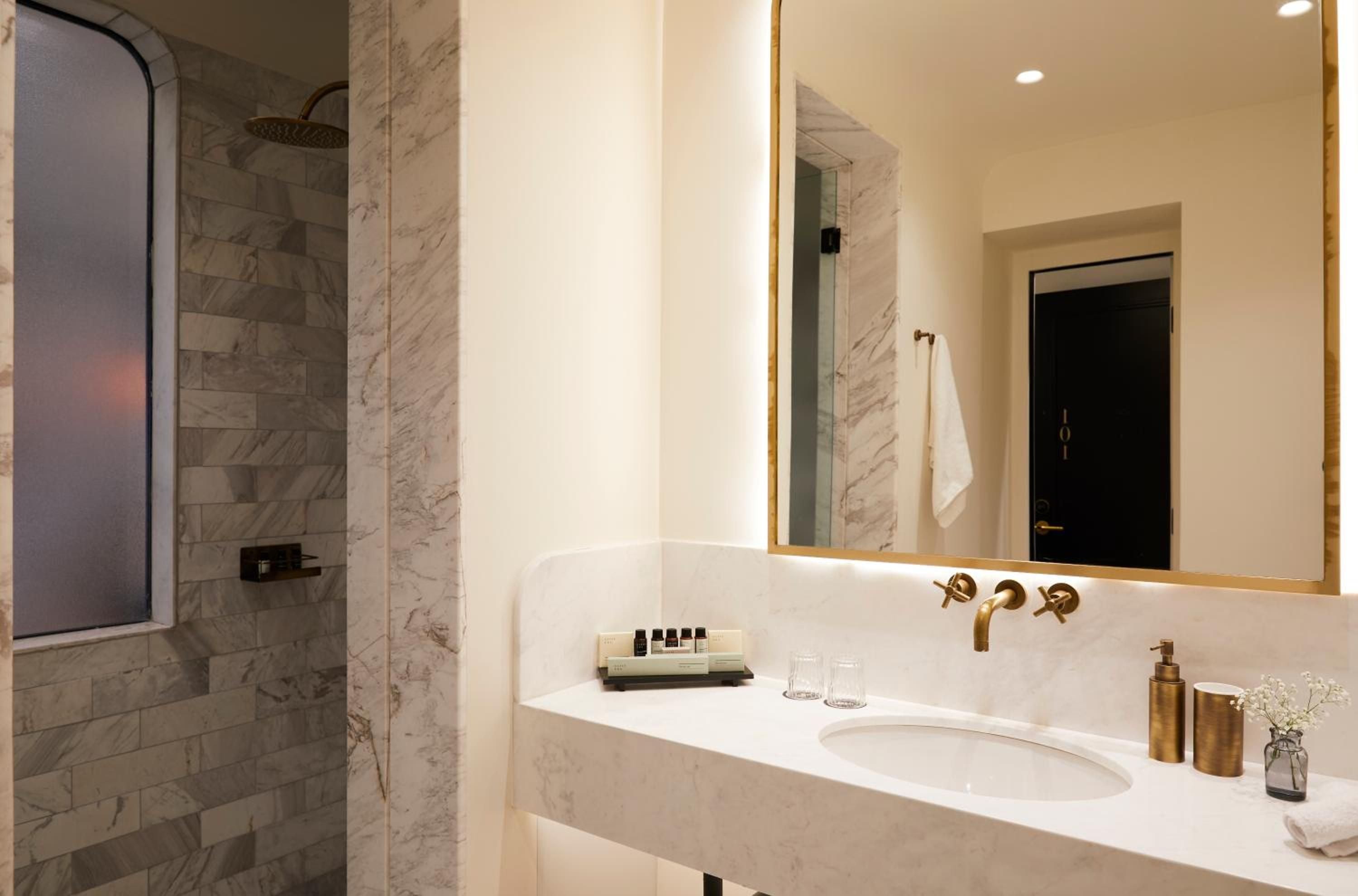 Marble veining flows across shower walls while brass fixtures catch warm light, creating an intimate sanctuary where luxury feels effortlessly understated.