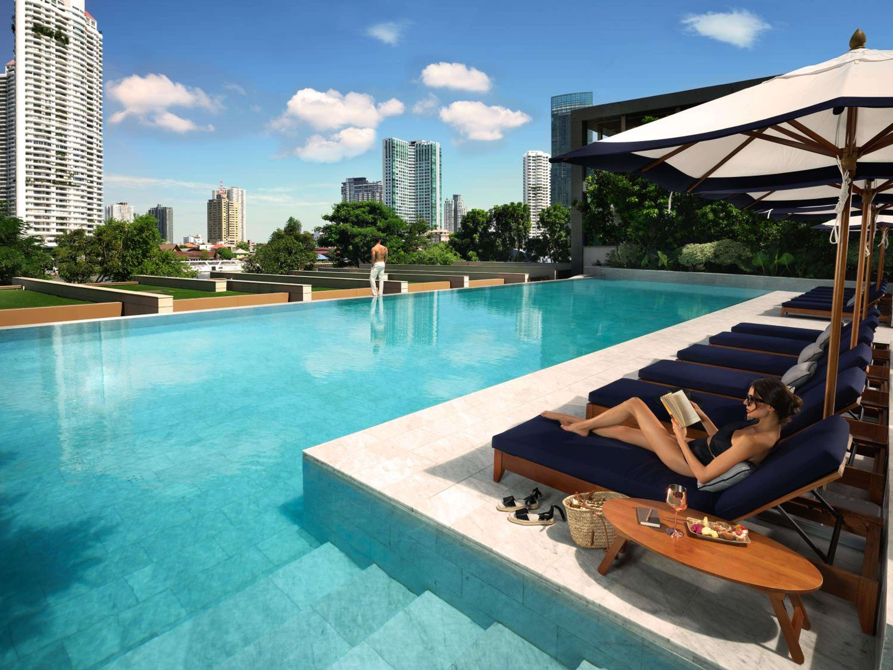 Azure waters stretch toward Bangkok's glittering skyline from this elevated sanctuary, where navy loungers and crisp umbrellas frame moments of urban serenity.