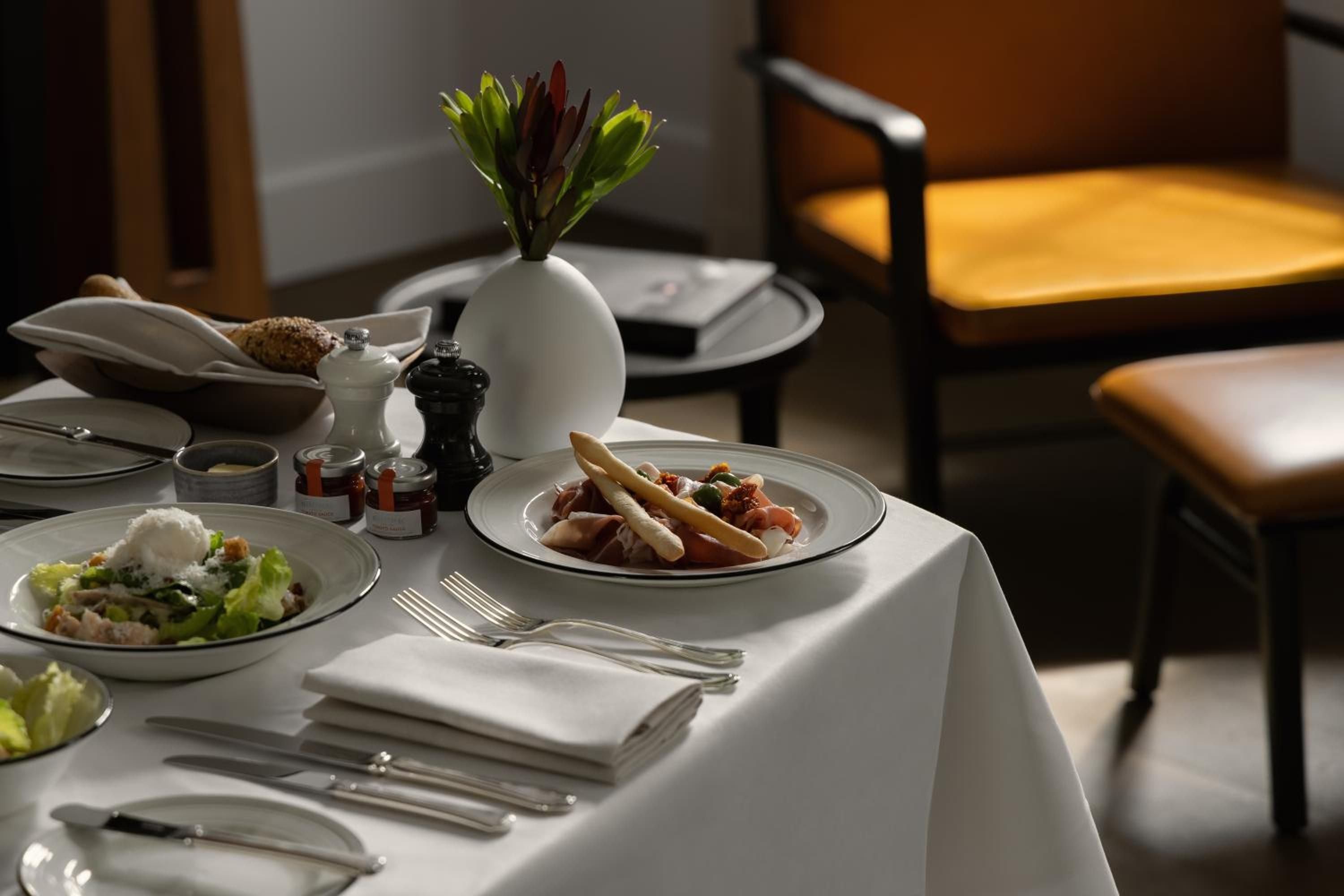 Crisp white linens frame artfully plated dishes at breakfast, where warm morning light filters across polished silverware and a delicate floral arrangement sets an intimate tone.