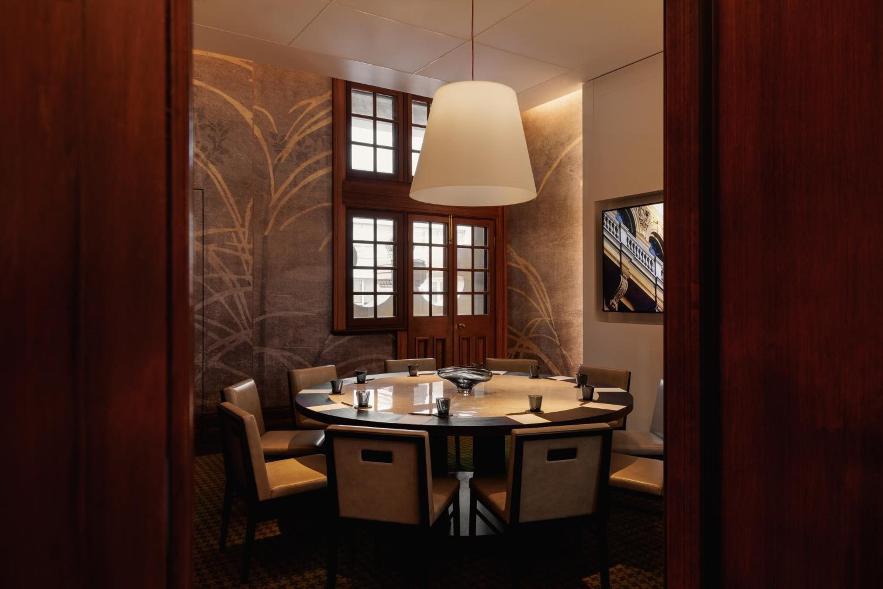 Intimate private dining unfolds beneath warm pendant lighting, where etched botanical murals and rich timber frames create an Asian-inspired sanctuary for memorable meals.