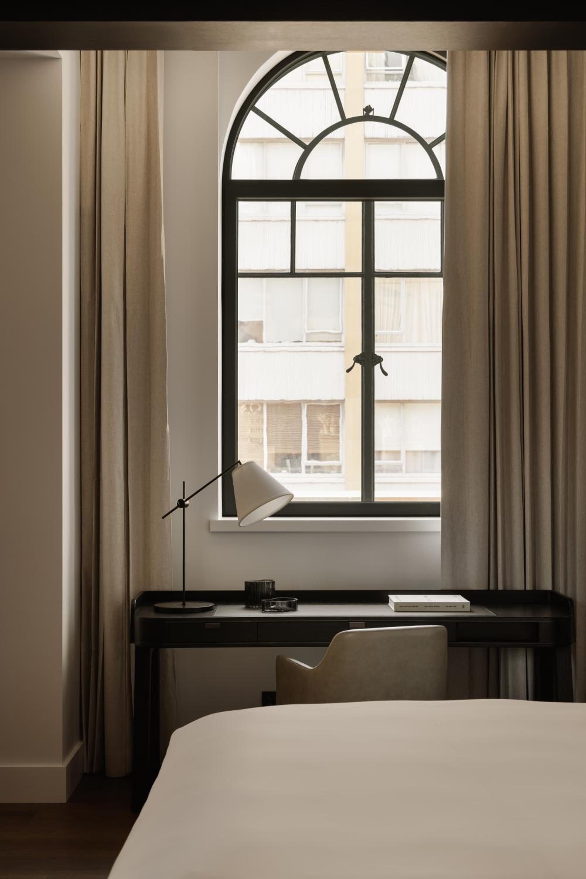Arched windows frame Sydney's heritage architecture while a sleek writing desk creates an intimate workspace where natural light dances across polished surfaces and cream linens.