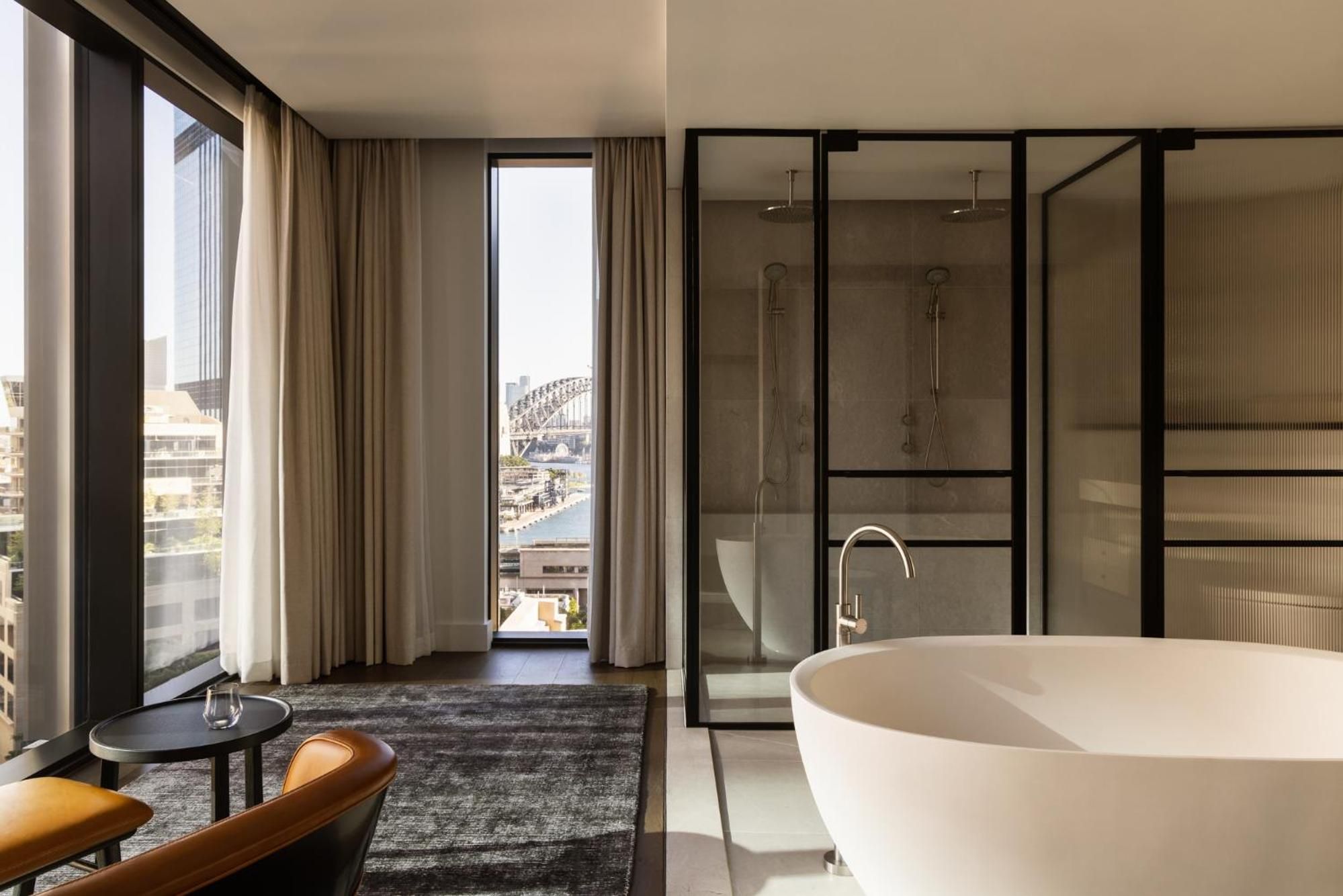 Floor-to-ceiling windows frame Sydney Harbour Bridge from this stunning suite, where a sculptural bathtub invites leisurely soaks amid sleek glass partitions and warm timber accents.