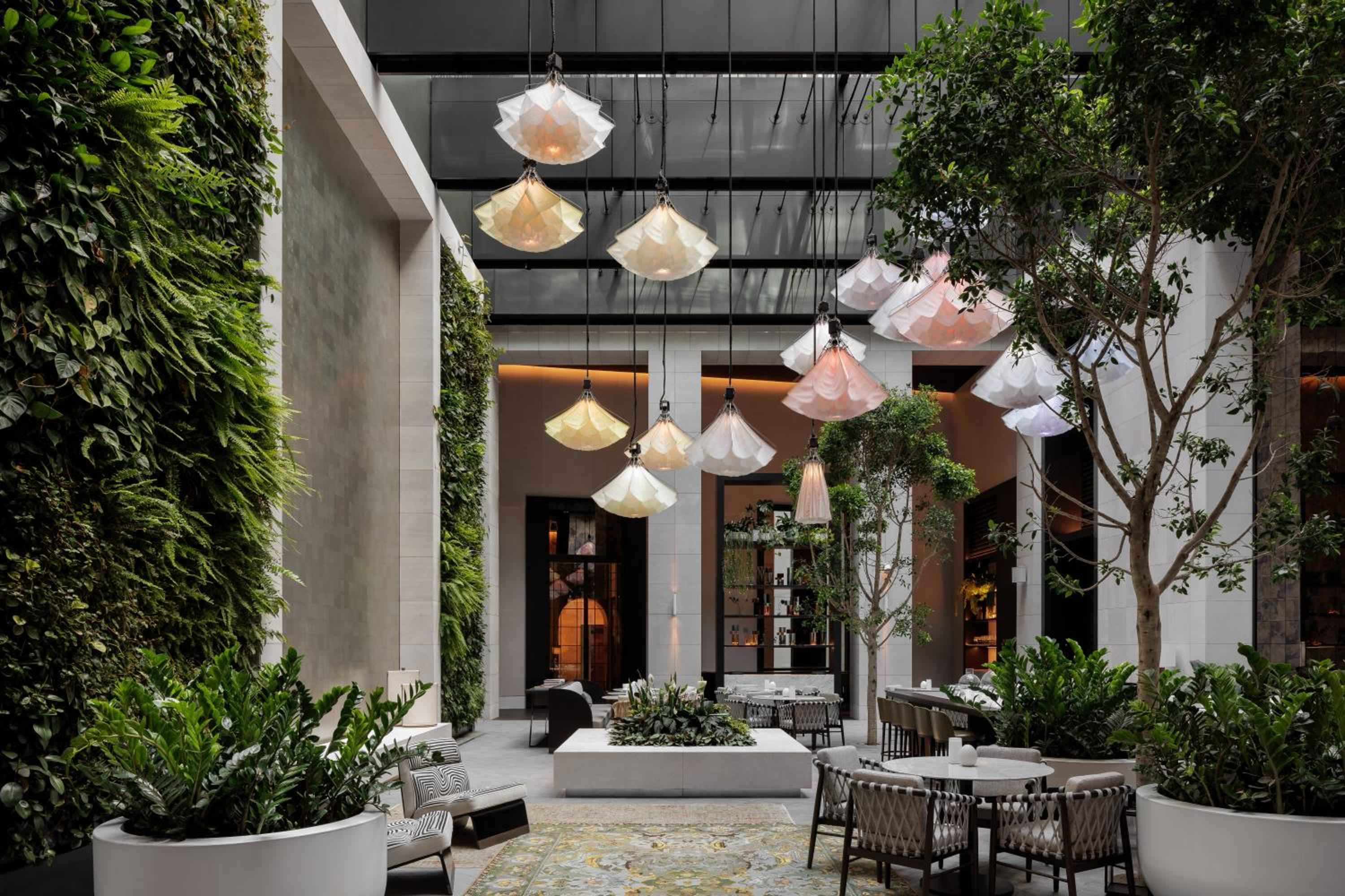 Sculptural pendant lights cascade like origami flowers above the verdant courtyard dining room, where living walls and heritage trees create an urban oasis.