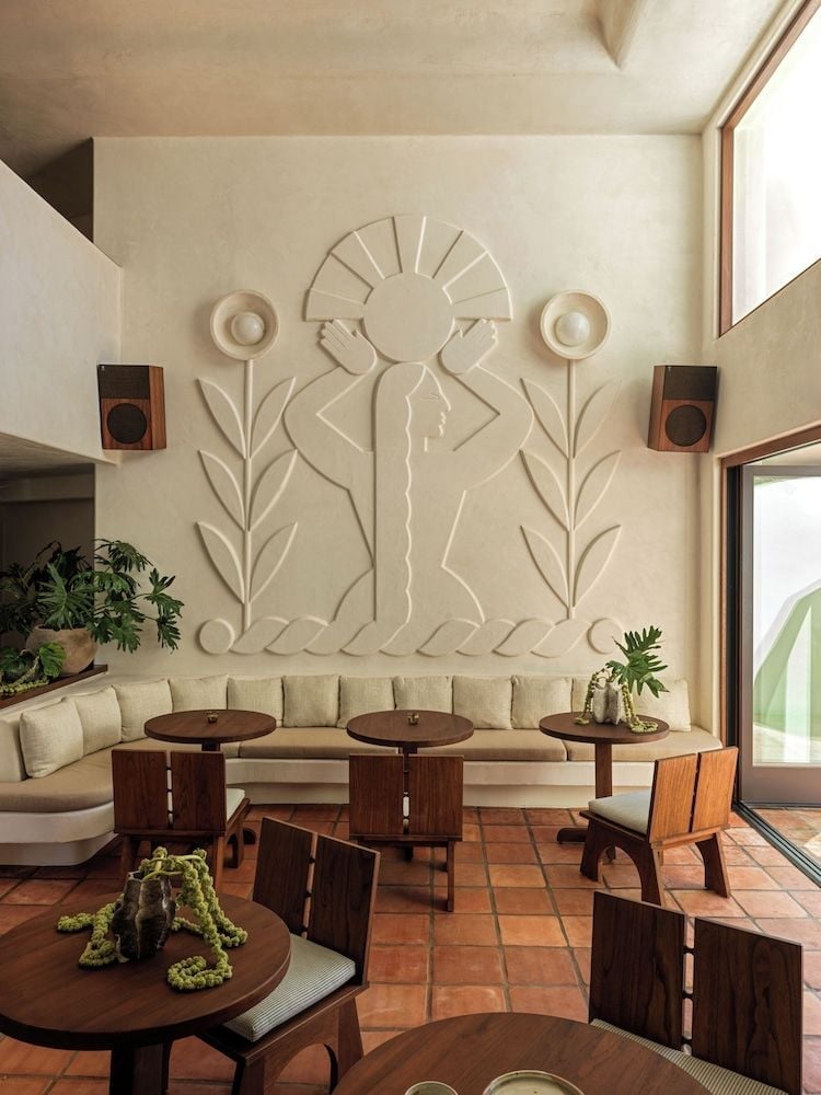 Sculptural bas-relief artwork crowns the restaurant's banquette seating, where terracotta tiles and rich wood furnishings create an intimate Mediterranean atmosphere bathed in golden light.