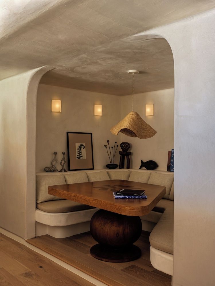 Curved adobe walls embrace an intimate dining nook where woven pendant lights cast golden pools over handcrafted furnishings and earthy ceramics.