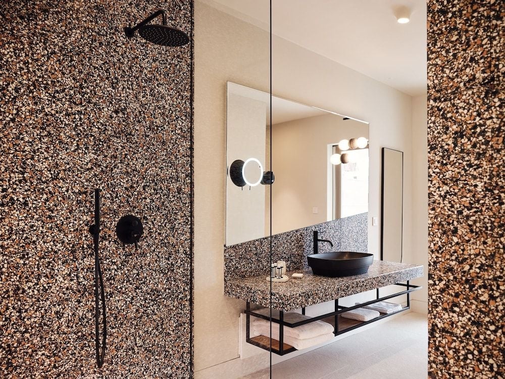 Crushed cork walls embrace the spa-like bathroom, where matte black fixtures and speckled stone create a cocoon of earthy luxury overlooking the vanity's sculptural basin.