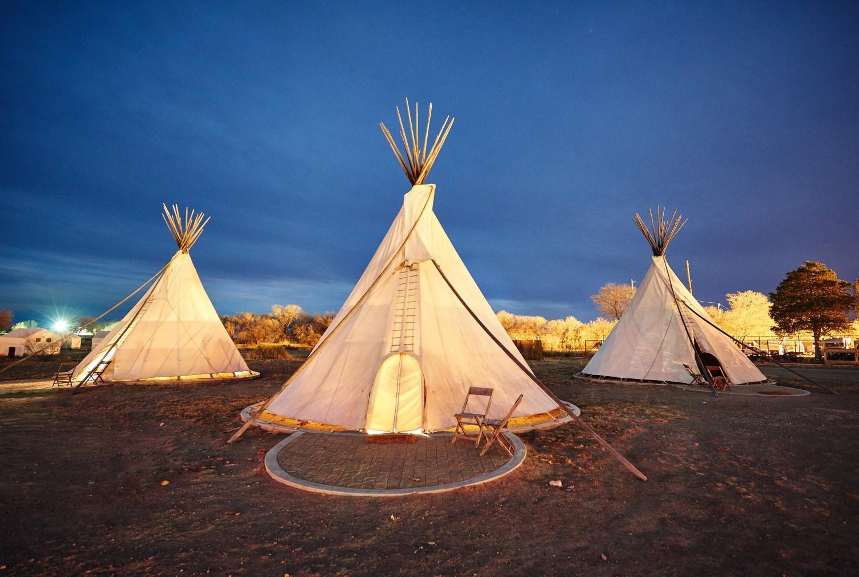 Canvas teepees glow like lanterns against the desert twilight, their wooden poles reaching skyward as golden hour light bathes this nomadic sanctuary in West Texas warmth.