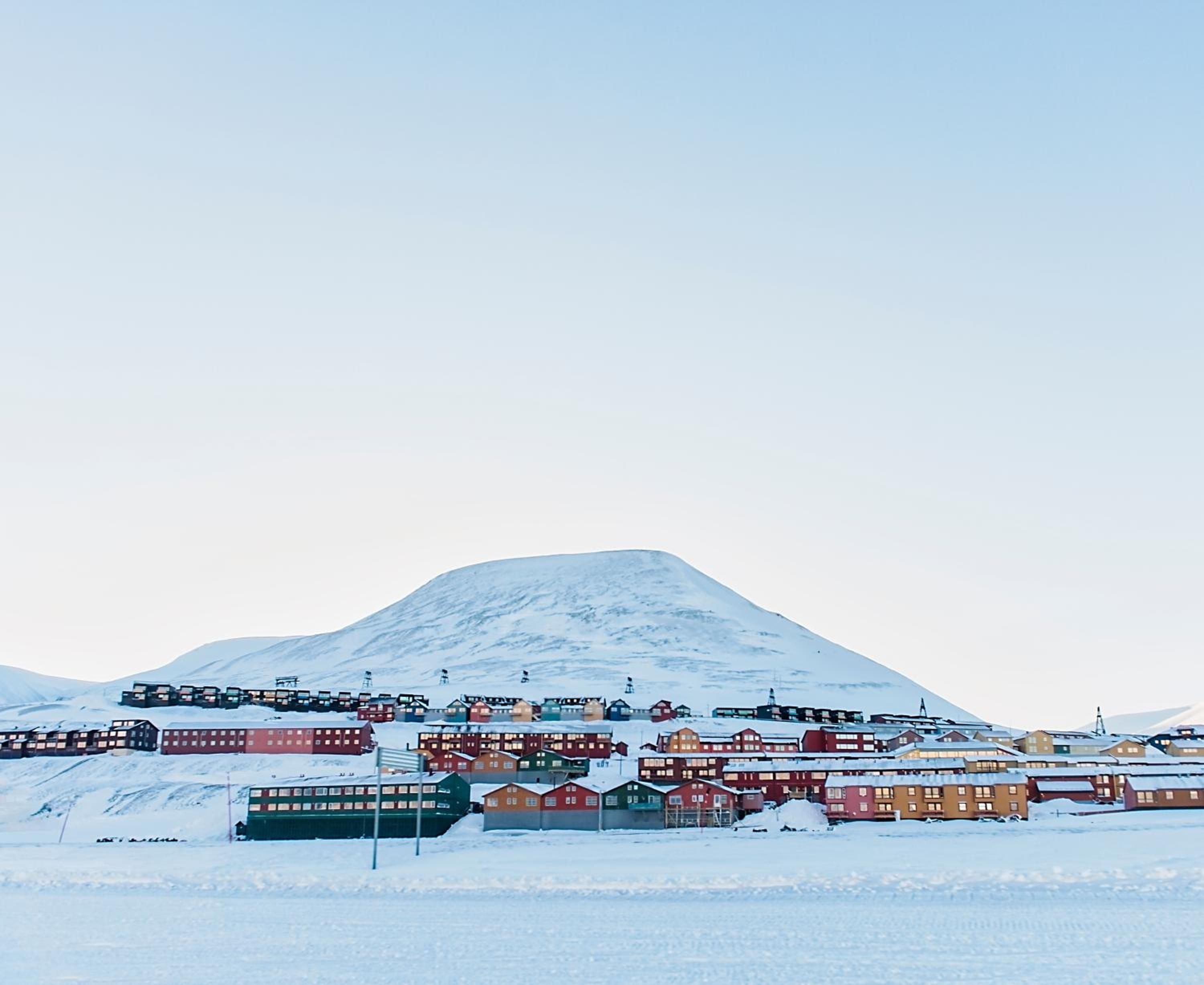 Colorful Nordic houses dot the snowy landscape beneath towering peaks, creating a fairy-tale Arctic settlement that feels both remote and wonderfully welcoming.