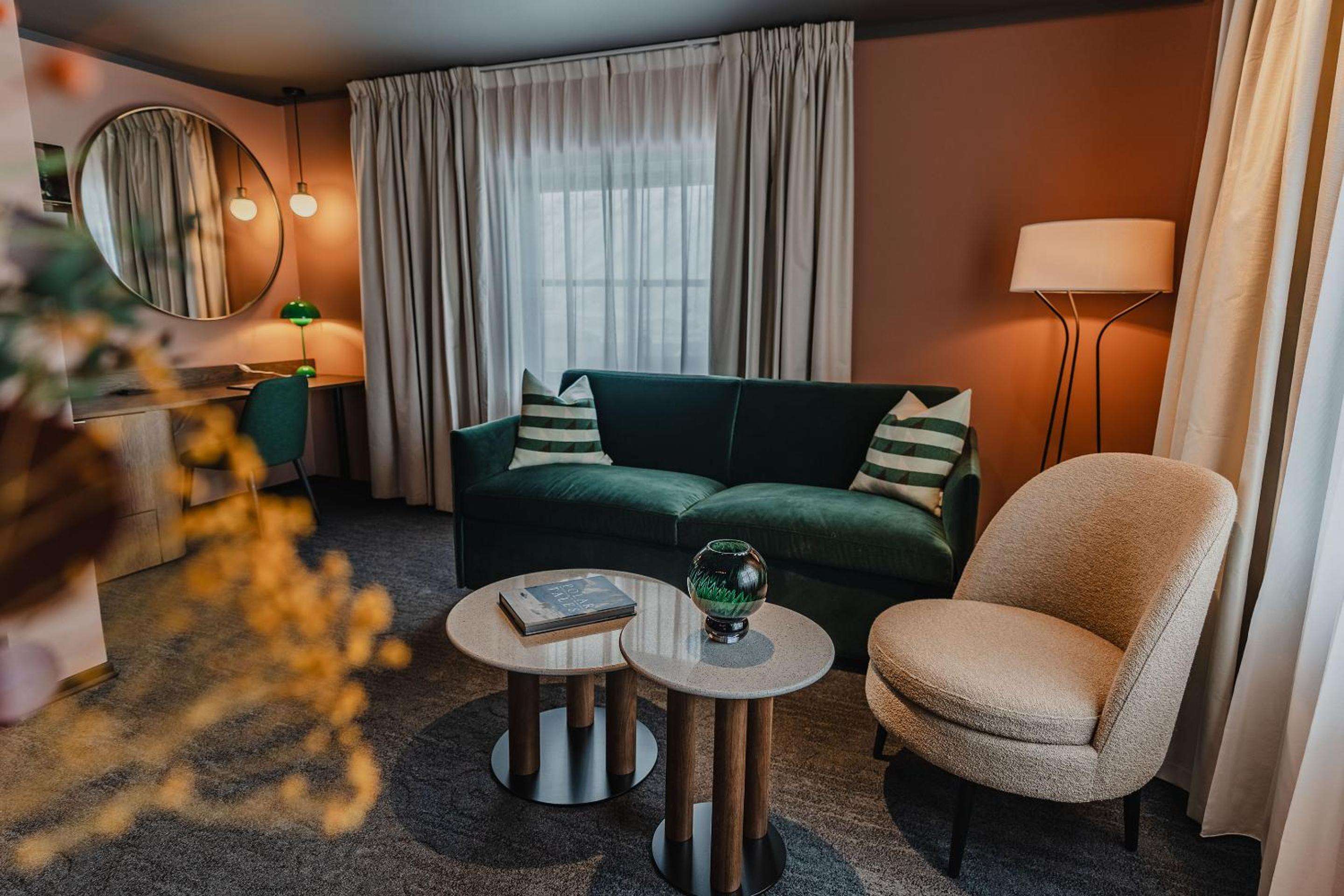 Emerald velvet sofas and warm terracotta walls create an inviting retreat, where Nordic minimalism meets alpine comfort in thoughtfully curated living spaces.