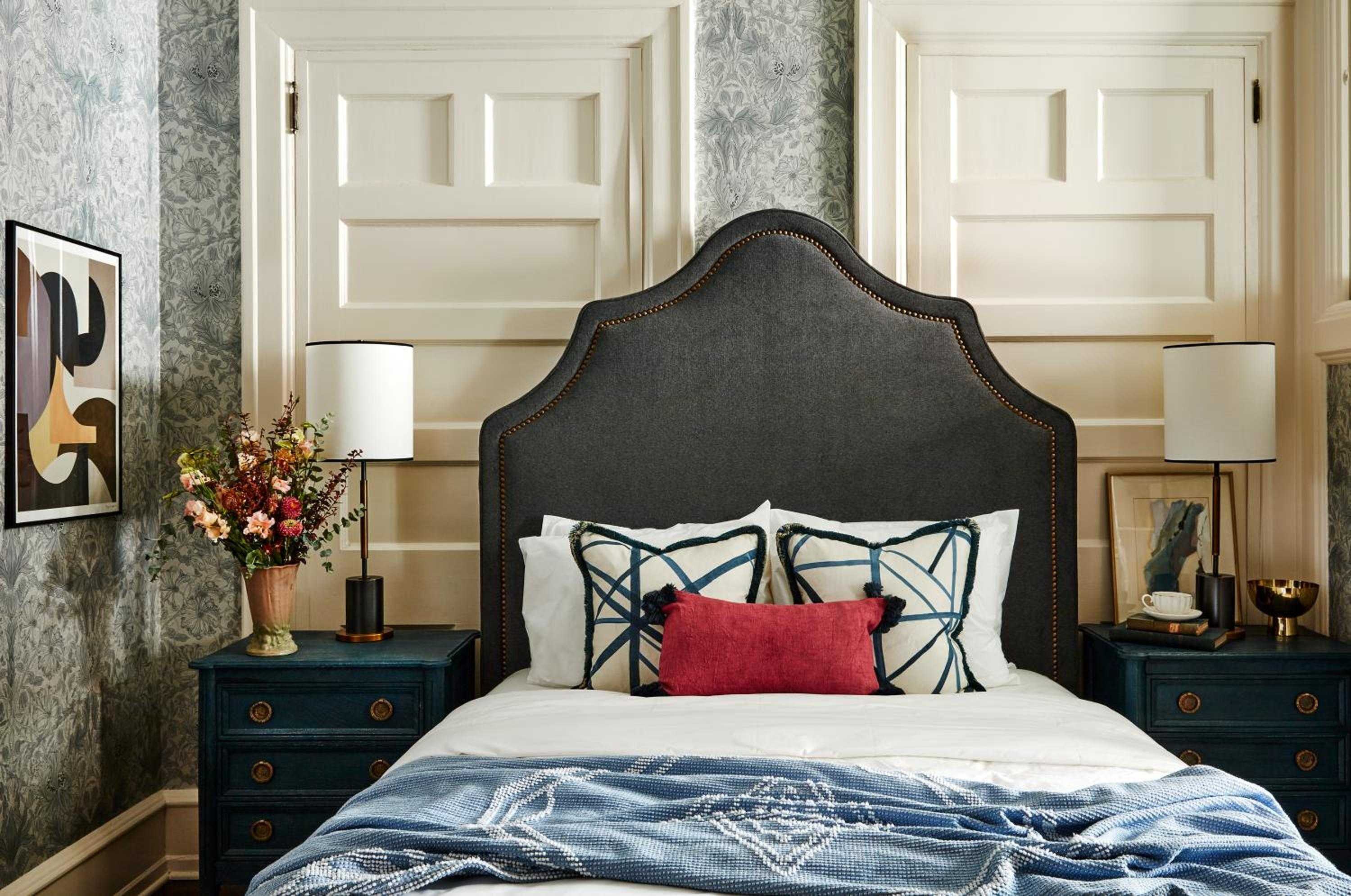 Charcoal headboard with brass nailheads anchors this sophisticated guest room, where navy geometric pillows and botanical wallpaper create timeless Philadelphia elegance.