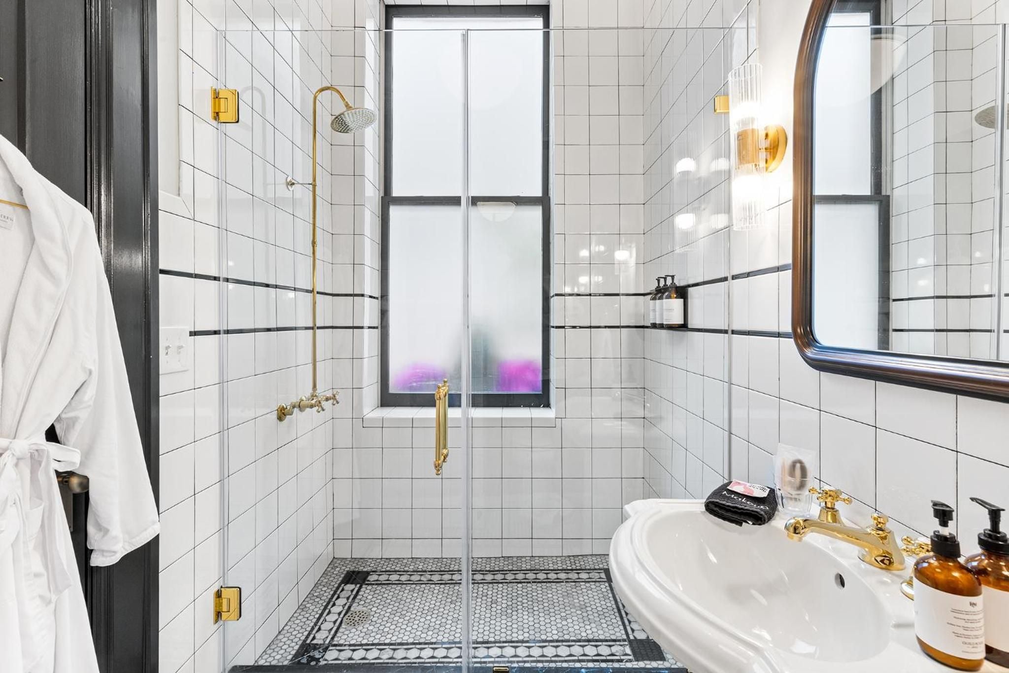 White subway tiles with charcoal grout create crisp geometric lines, while brass fixtures and a porthole mirror add nautical sophistication to this thoughtfully appointed bathroom.