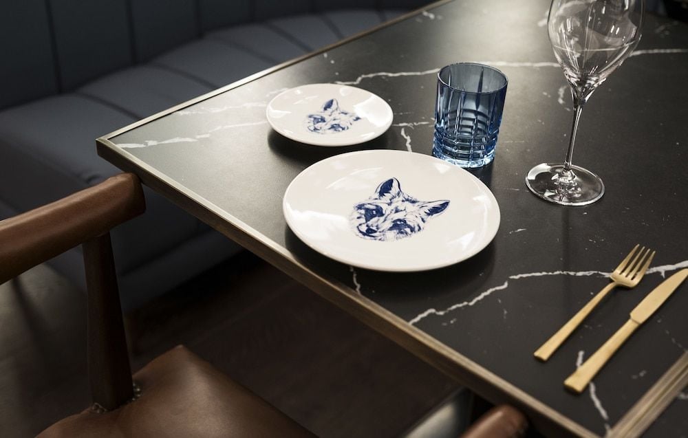 Blue-and-white porcelain featuring whimsical animal motifs sets an intimate tone against the sleek marble table, where golden cutlery catches afternoon light streaming through the dining room.