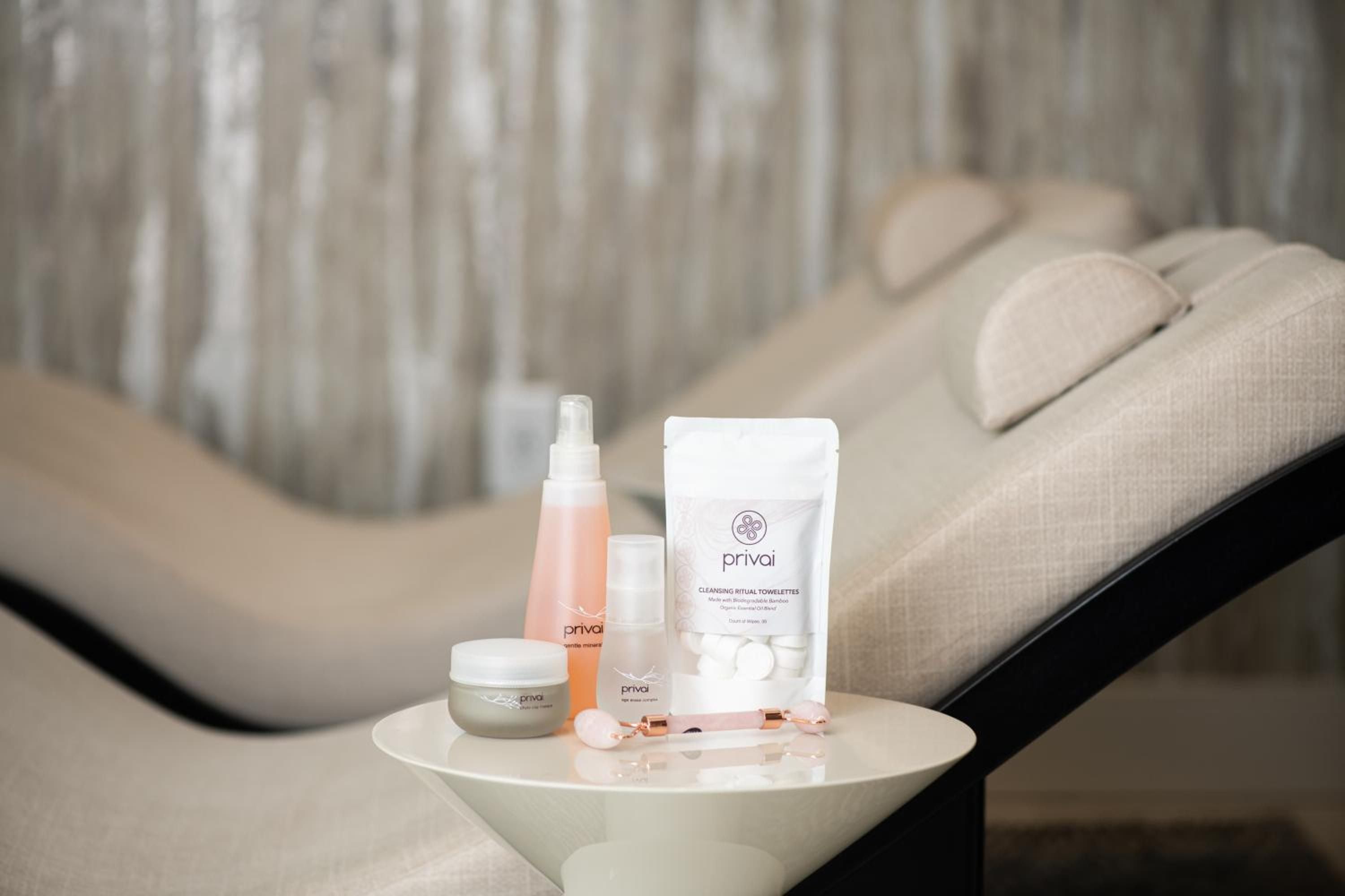 Privai skincare products rest artfully on a curved white table beside plush spa seating, creating an intimate wellness sanctuary bathed in soft natural light.