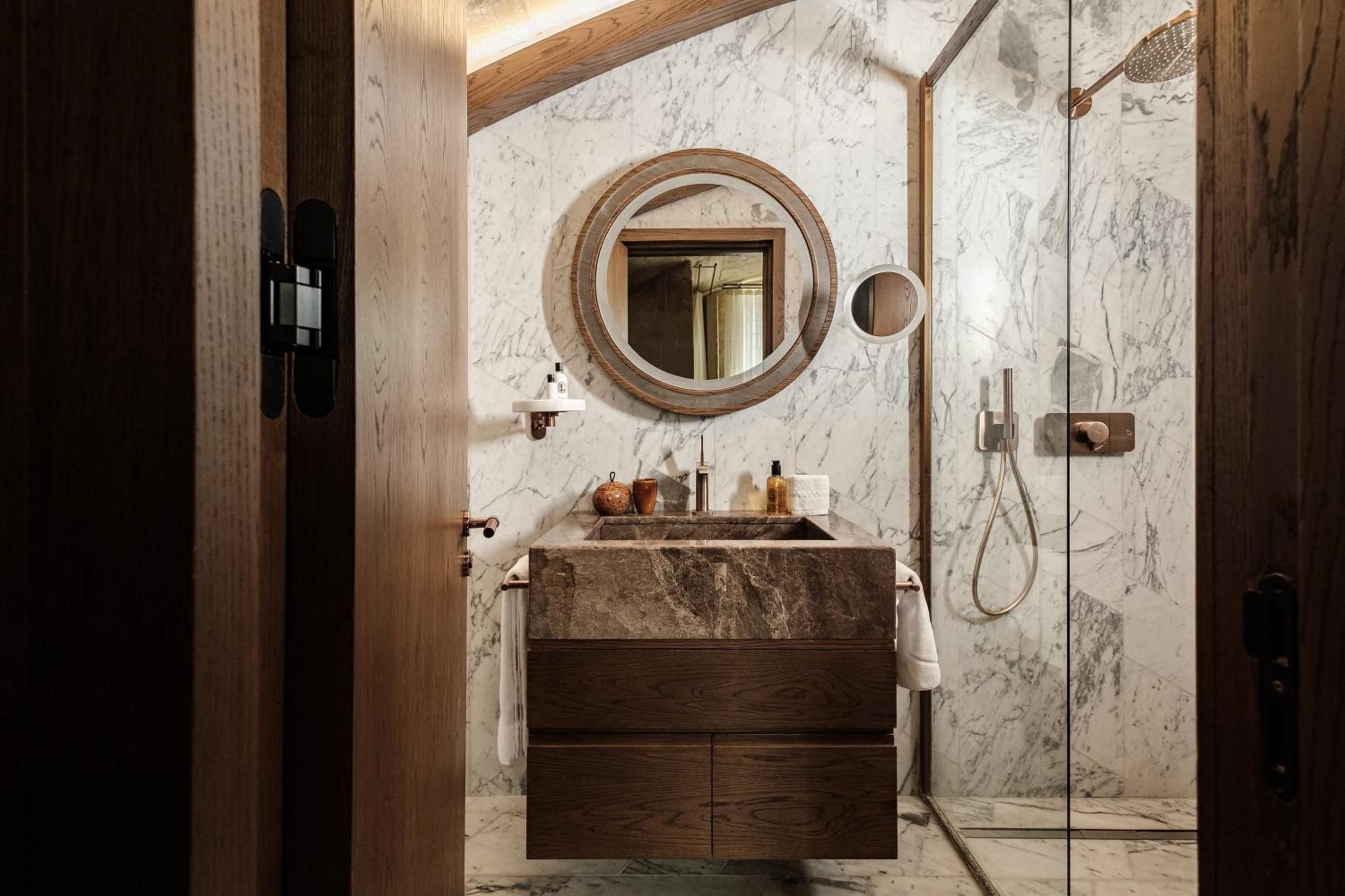 Warm wood meets cool marble in this sculptural sanctuary, where circular mirrors frame intimate moments and natural textures create a spa-like cocoon of luxury.