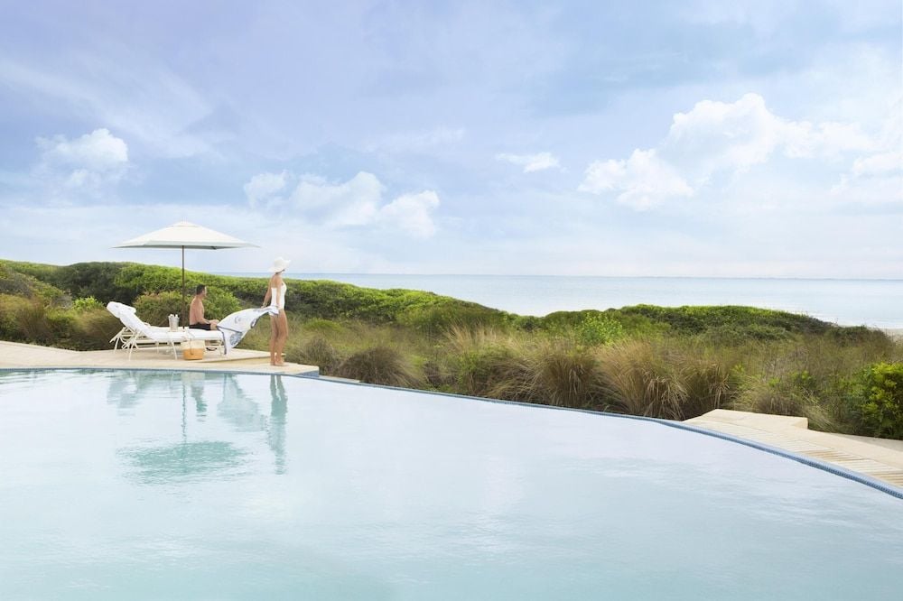 An infinity pool seems to float above coastal dunes, where salt-kissed breezes meet crystalline waters and the Atlantic horizon stretches endlessly beyond native grasses.
