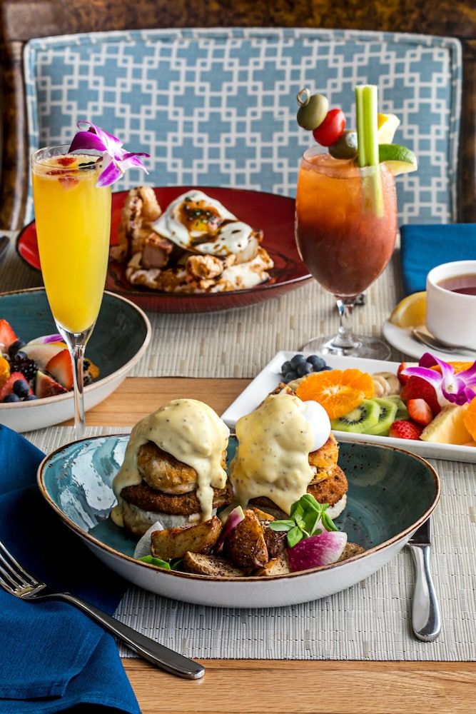 Elevated brunch artistry unfolds with perfectly poached eggs benedict alongside craft cocktails garnished with tropical orchids, creating an indulgent oceanside dining ritual.