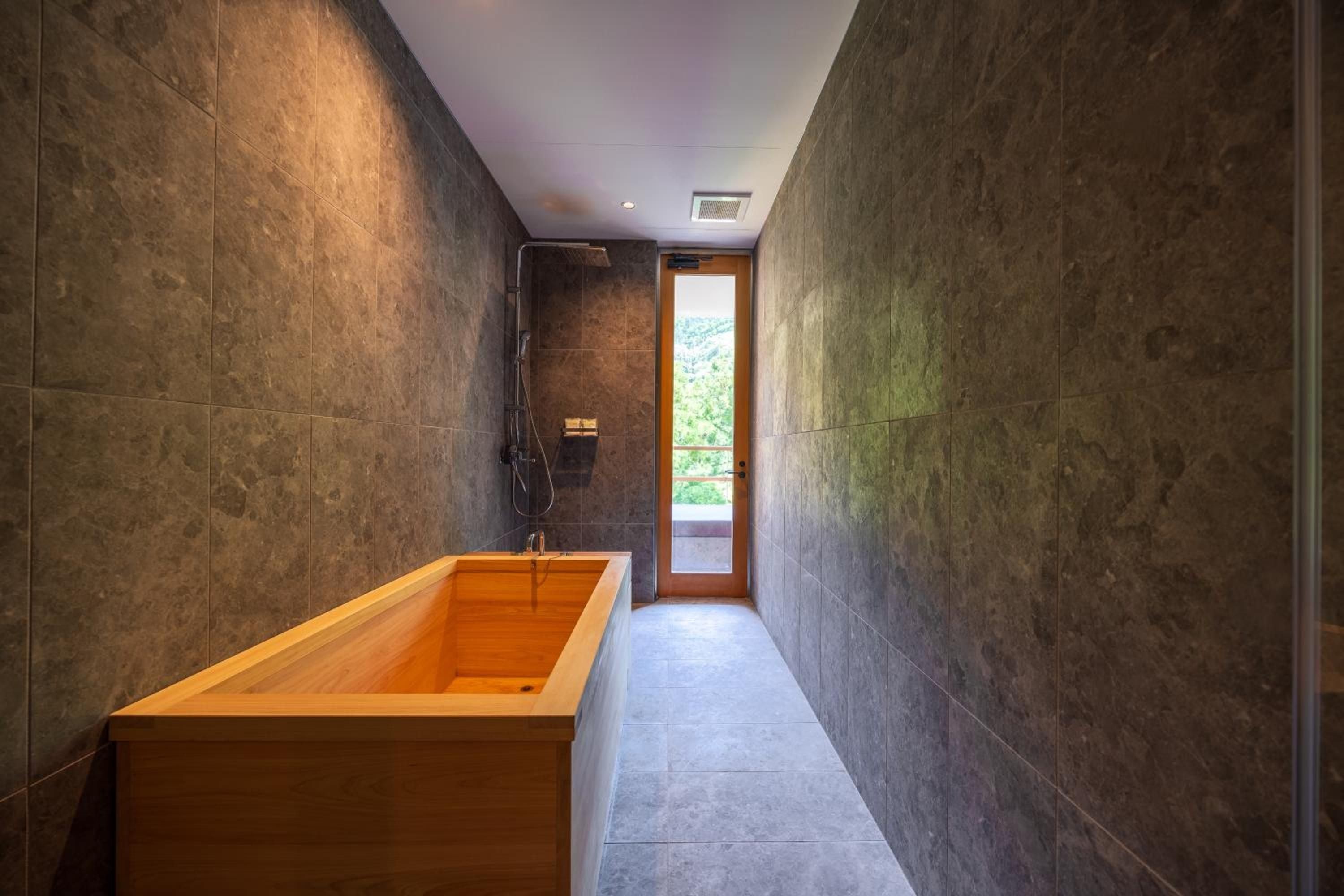 Charcoal stone walls embrace a gleaming hinoki wood soaking tub, where modern minimalism meets traditional Japanese bathing rituals in this serene sanctuary.