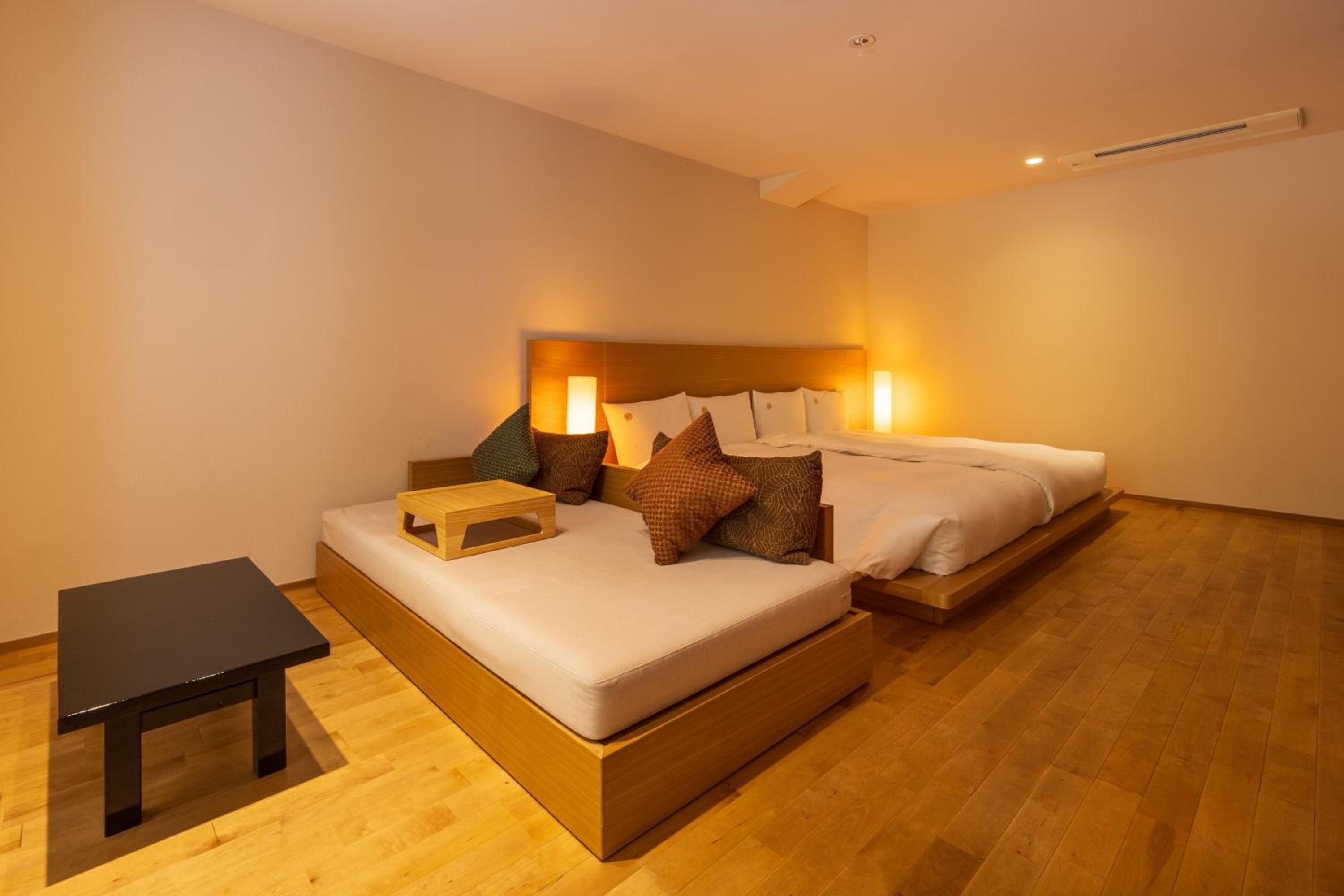 Warm wooden floors and amber lighting create an intimate sanctuary, where textured pillows and minimalist design blur the lines between traditional Japanese aesthetics and modern luxury.