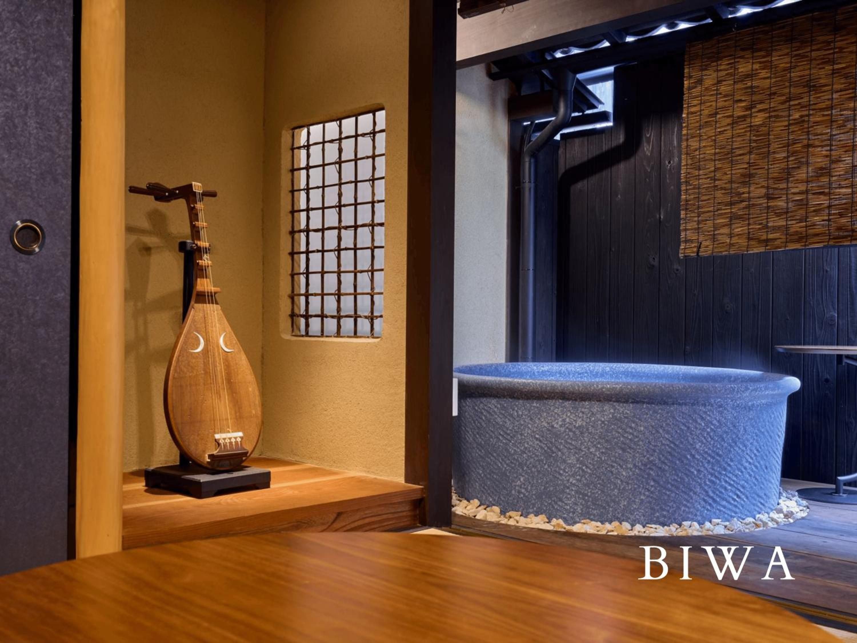 Warm wood tones and a traditional biwa create intimate ambiance around the circular stone soaking tub, where bamboo screens filter gentle light through this serene bathing sanctuary.