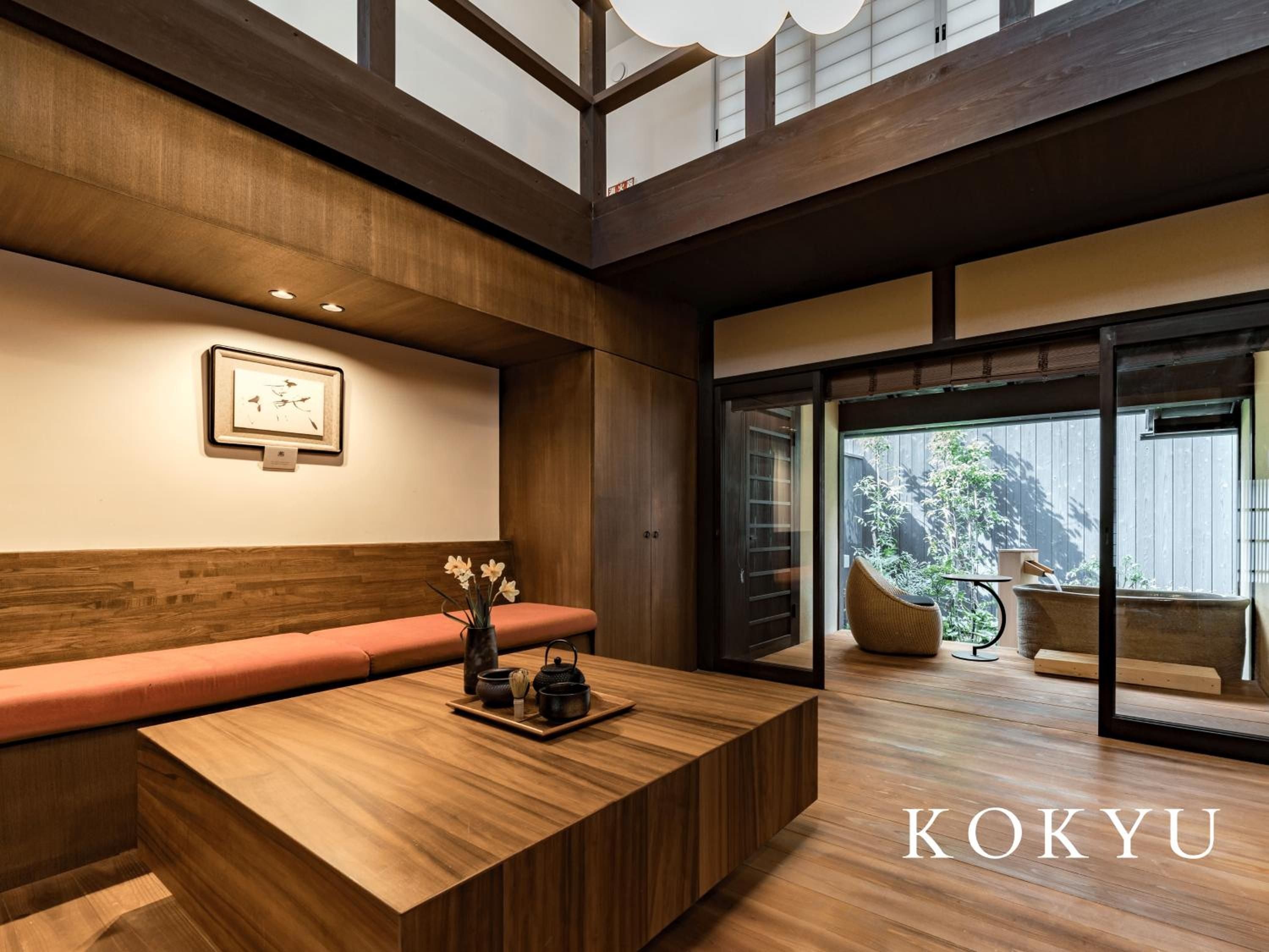 Warm wood beams frame this intimate living space where traditional tatami meets modern comfort, overlooking a private garden through sliding glass doors.
