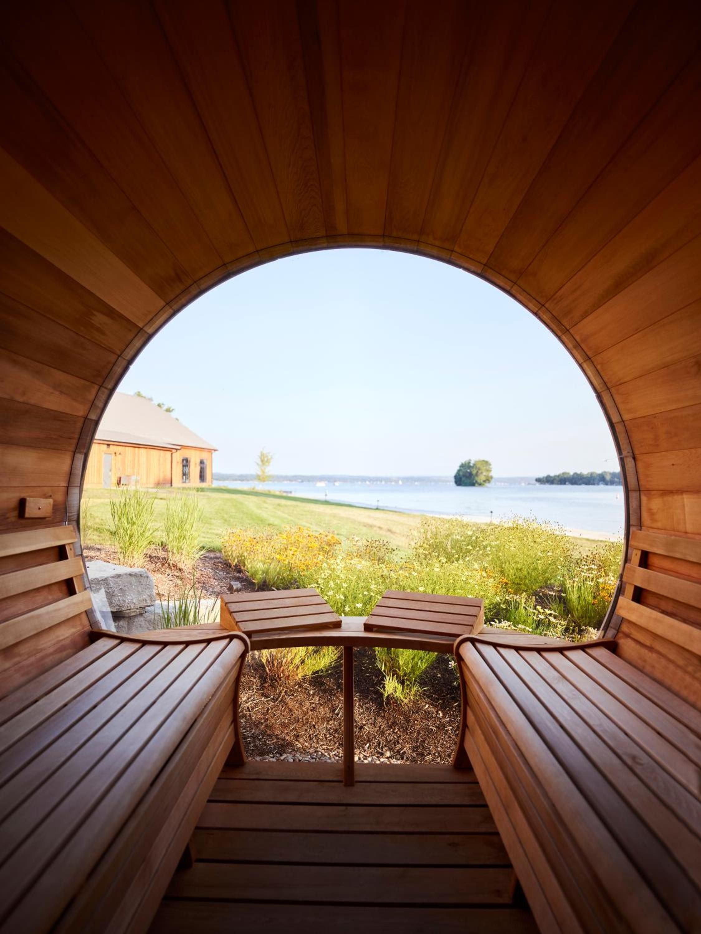 Cedar-lined sauna frames Canandaigua Lake's shimmering waters through its distinctive barrel window, creating an intimate wellness sanctuary where warm wood meets cool lake breezes.