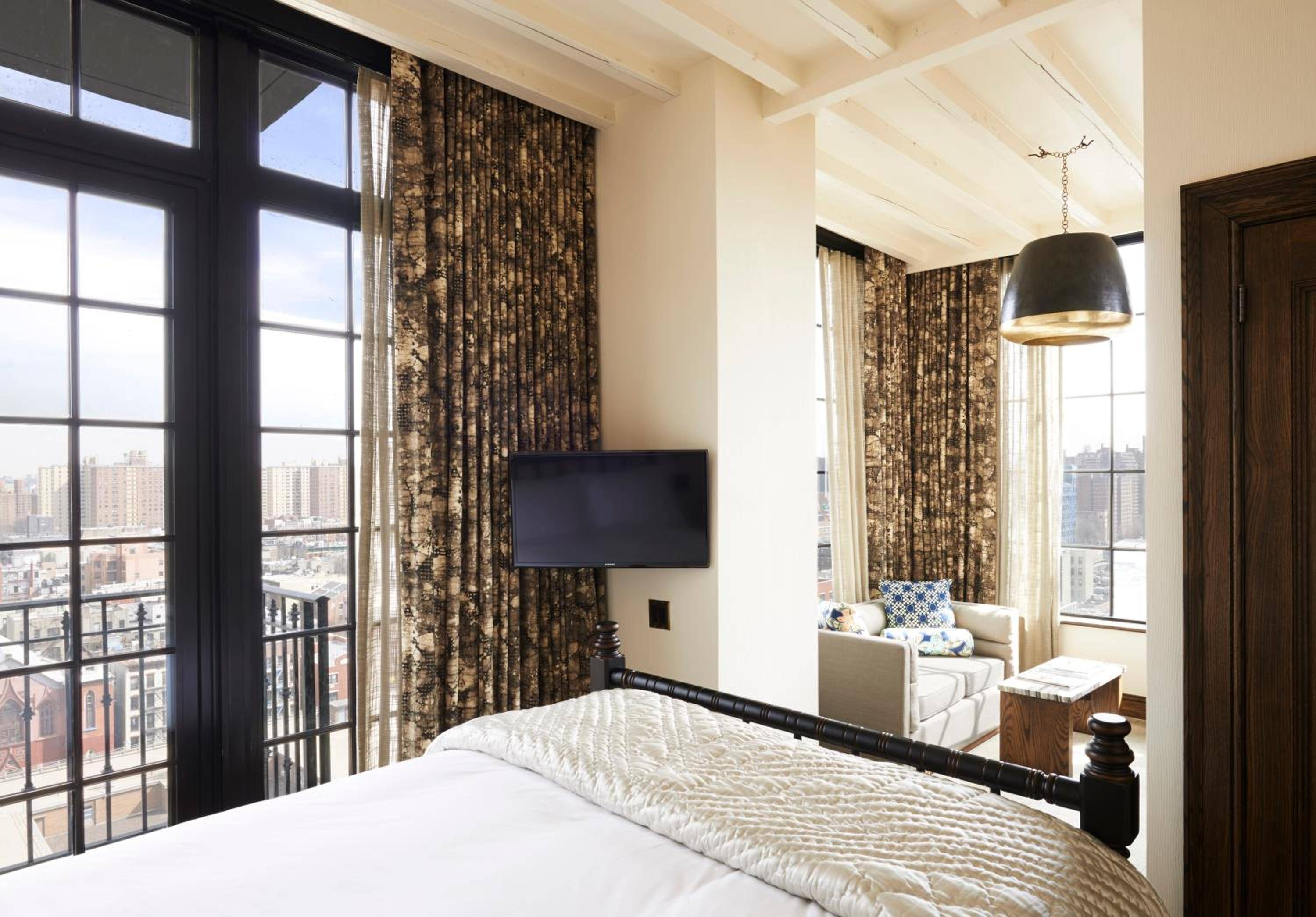 Exposed beams frame Manhattan vistas through floor-to-ceiling windows, while rich tapestry curtains and contemporary furnishings create an intimate retreat high above the Lower East Side.