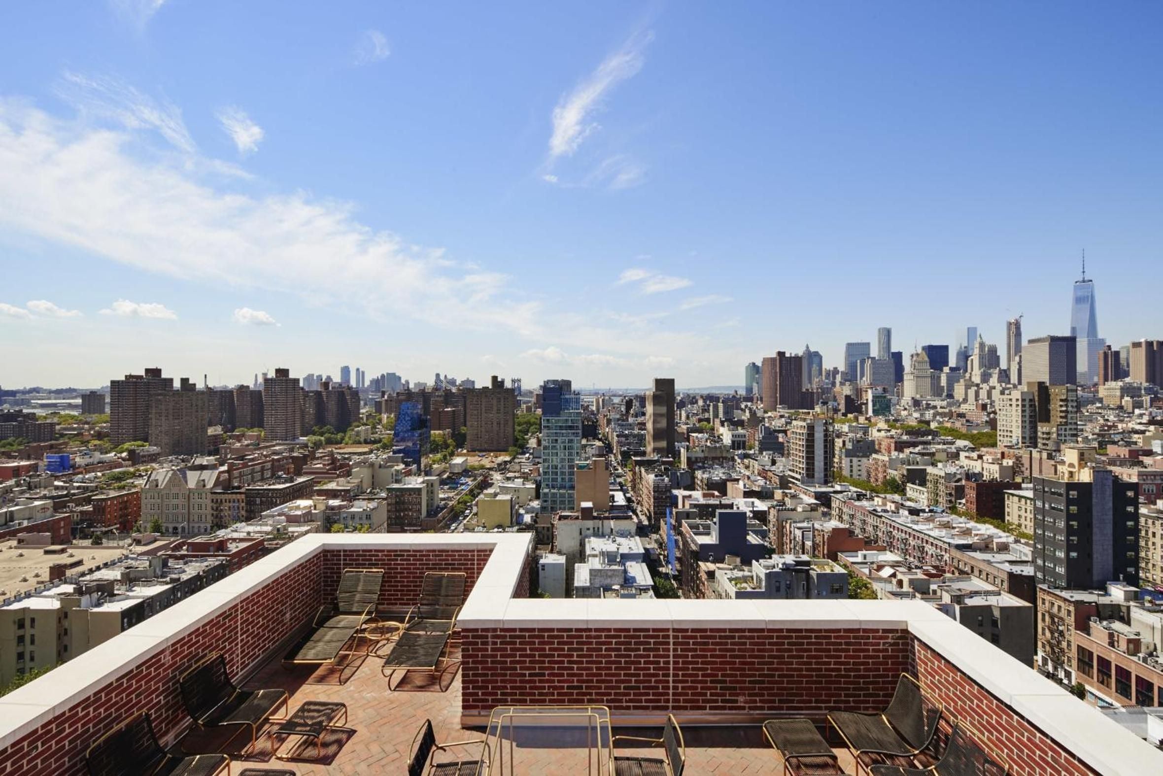 Sweeping Manhattan vistas unfold from the brick-walled rooftop terrace, where weathered wooden furniture frames iconic downtown skyline views stretching toward One World Trade Center.