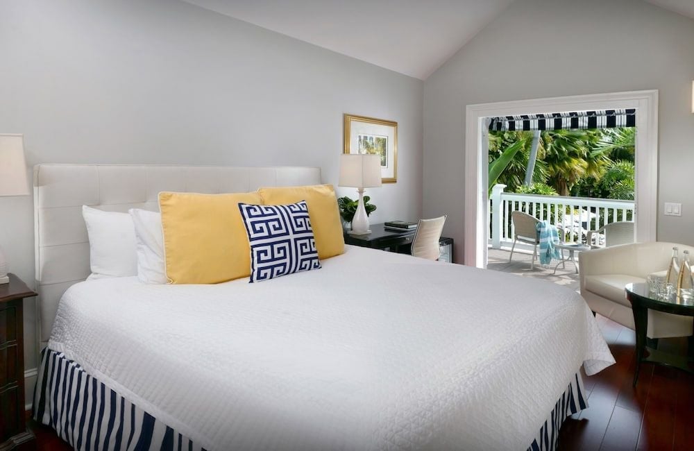 Crisp white linens and navy Greek key pillows create coastal elegance in this poolside suite, where French doors open to tropical breezes and swaying palms.