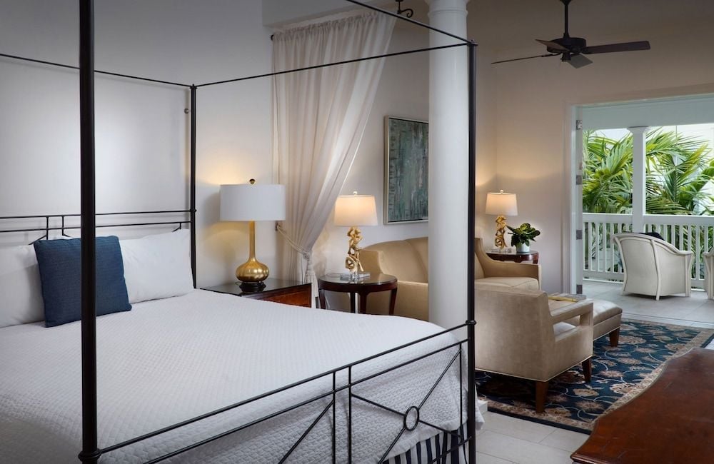 Wrought-iron four-poster frames invite tropical breezes through billowing curtains, while polished hardwood floors and golden lamplight create an intimate sanctuary overlooking swaying palms.
