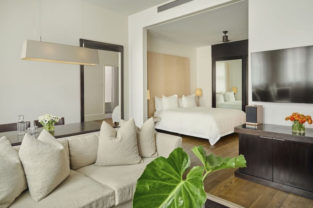 Warm wood floors and linen seating create an inviting living space that flows seamlessly into the serene bedroom, where natural light filters through sleek architectural lines.