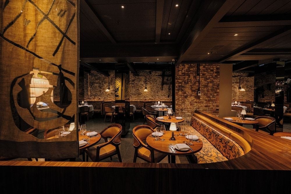 Exposed brick walls and sculptural metal artwork create an intimate dining atmosphere, where candlelit tables and warm amber lighting invite lingering conversations over exceptional cuisine.