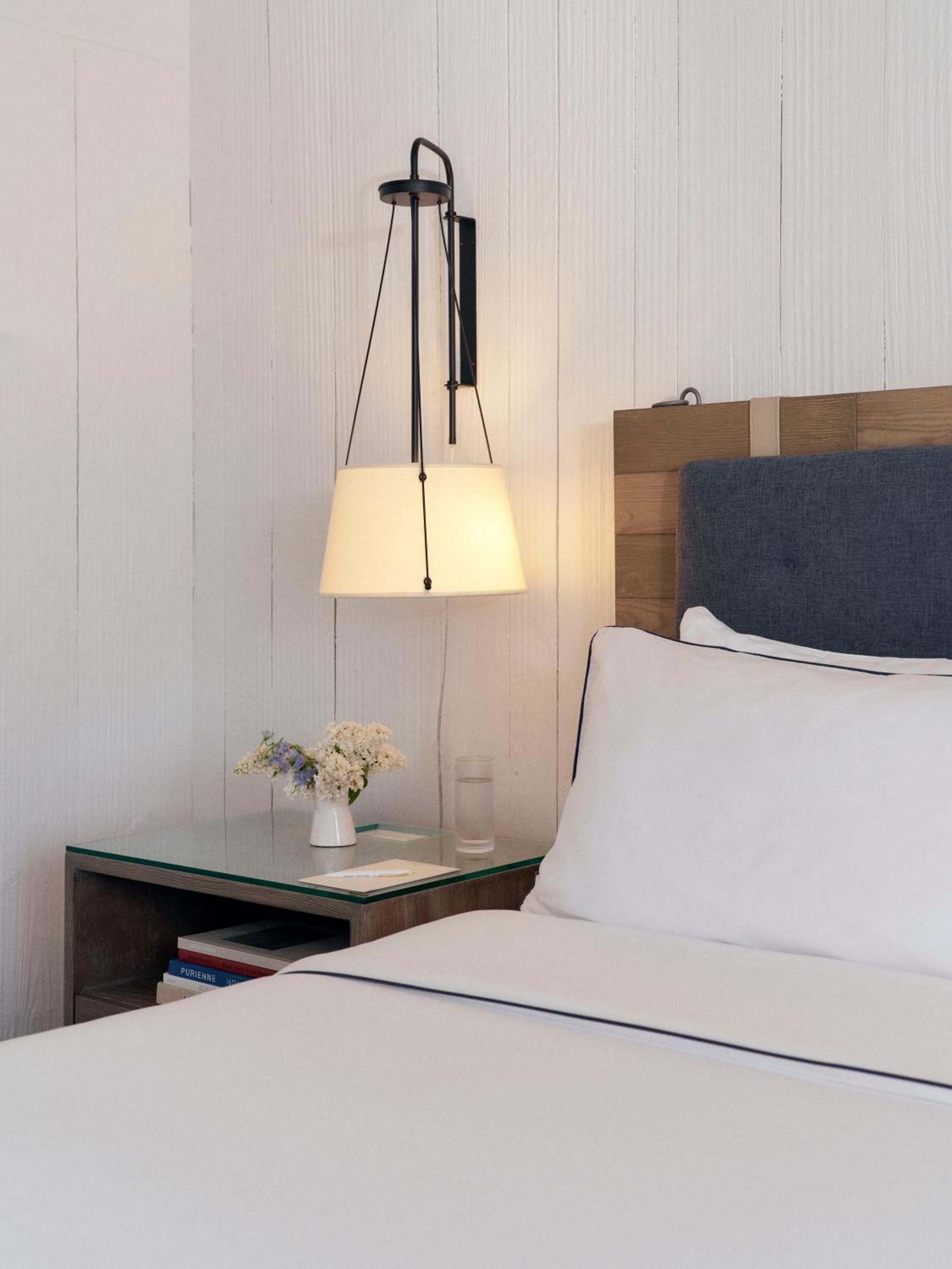 Nautical-inspired bedside details blend weathered wood headboards with crisp white linens, while pendant lighting casts a warm glow over fresh hydrangeas and glass-topped nightstands.