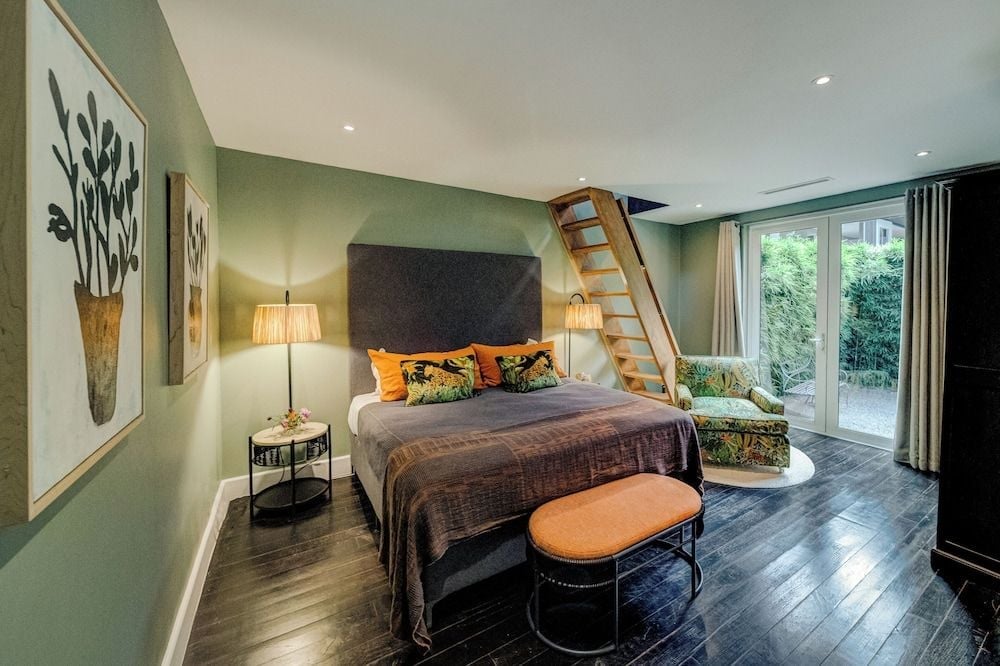 Sage-green walls and charcoal linens create a cocoon of calm, while orange accent pillows and vintage botanical prints add warmth to this thoughtfully curated sanctuary.