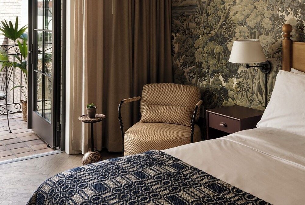 Botanical wallpaper and rich textures create an intimate reading corner, where afternoon light filters through French doors onto handwoven throws and polished wood.